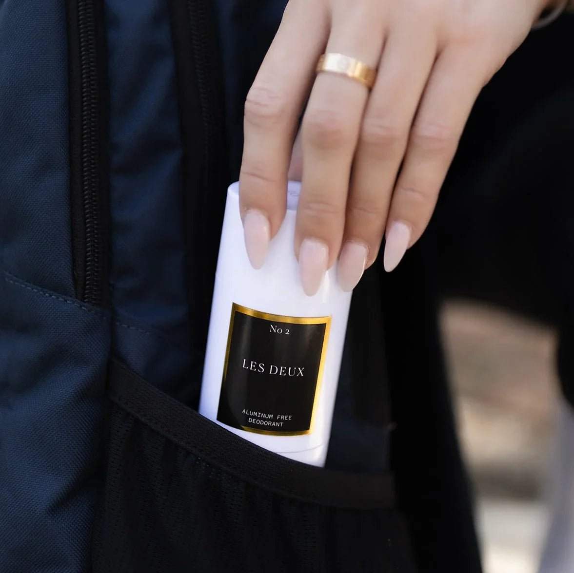 White plastic stick deodorant with black and gold label, held by a hand with light pink nails, labeled aluminum free deodorant.
