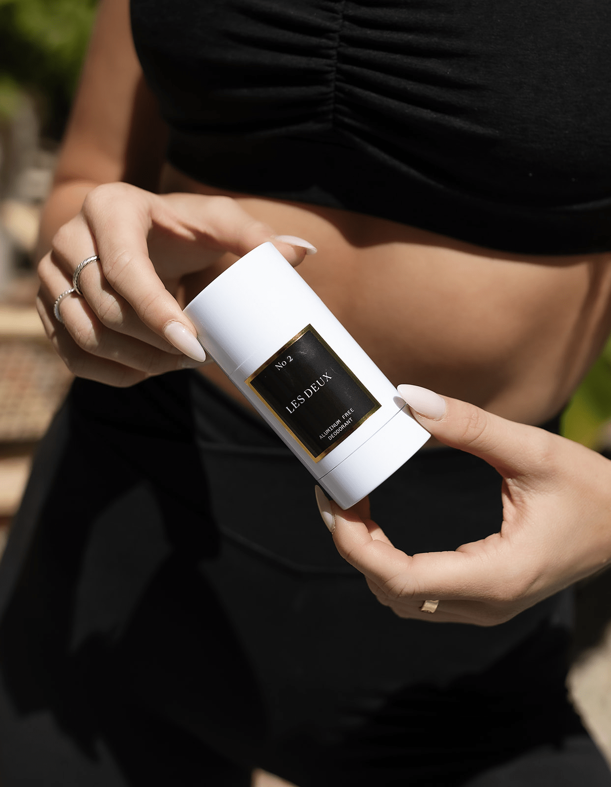 White plastic aluminum free deodorant stick with a black and gold label held by a person in black clothing