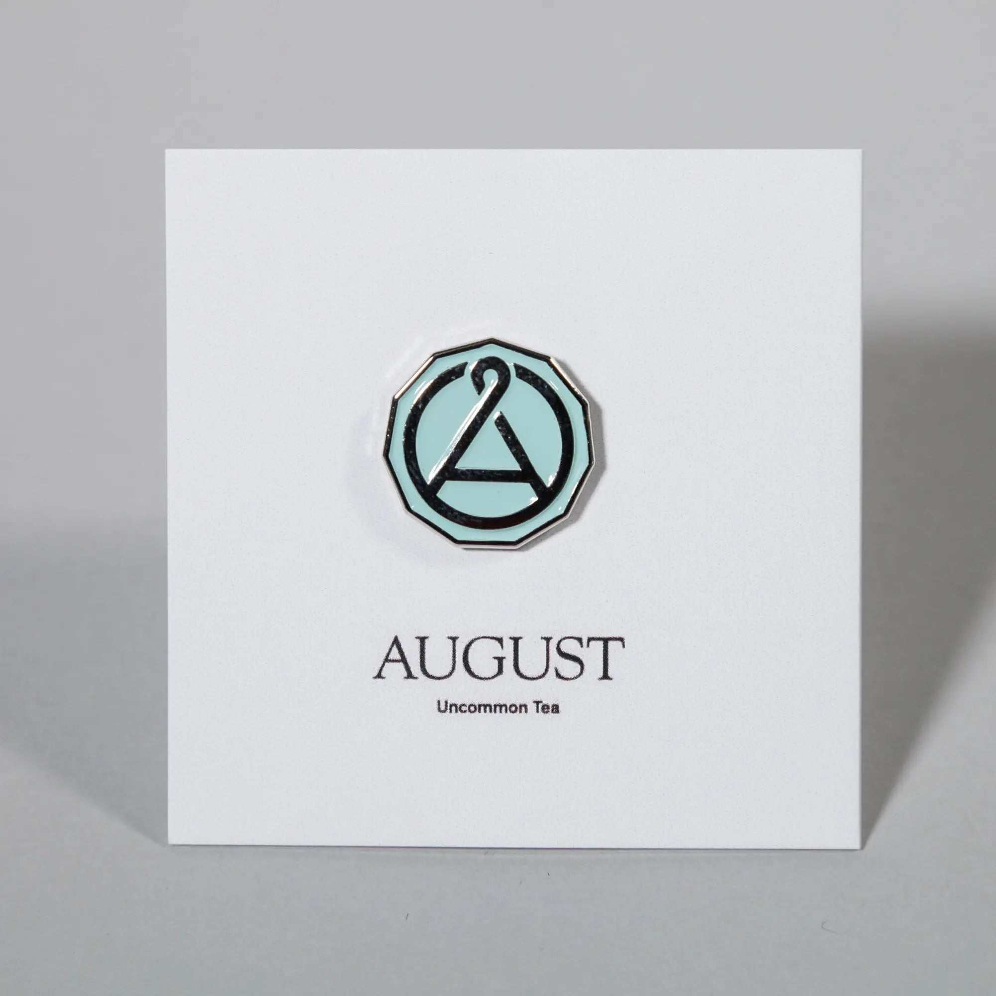 August Seal Enamel Pin with a mint green center, chrome outline and black geometric seal design