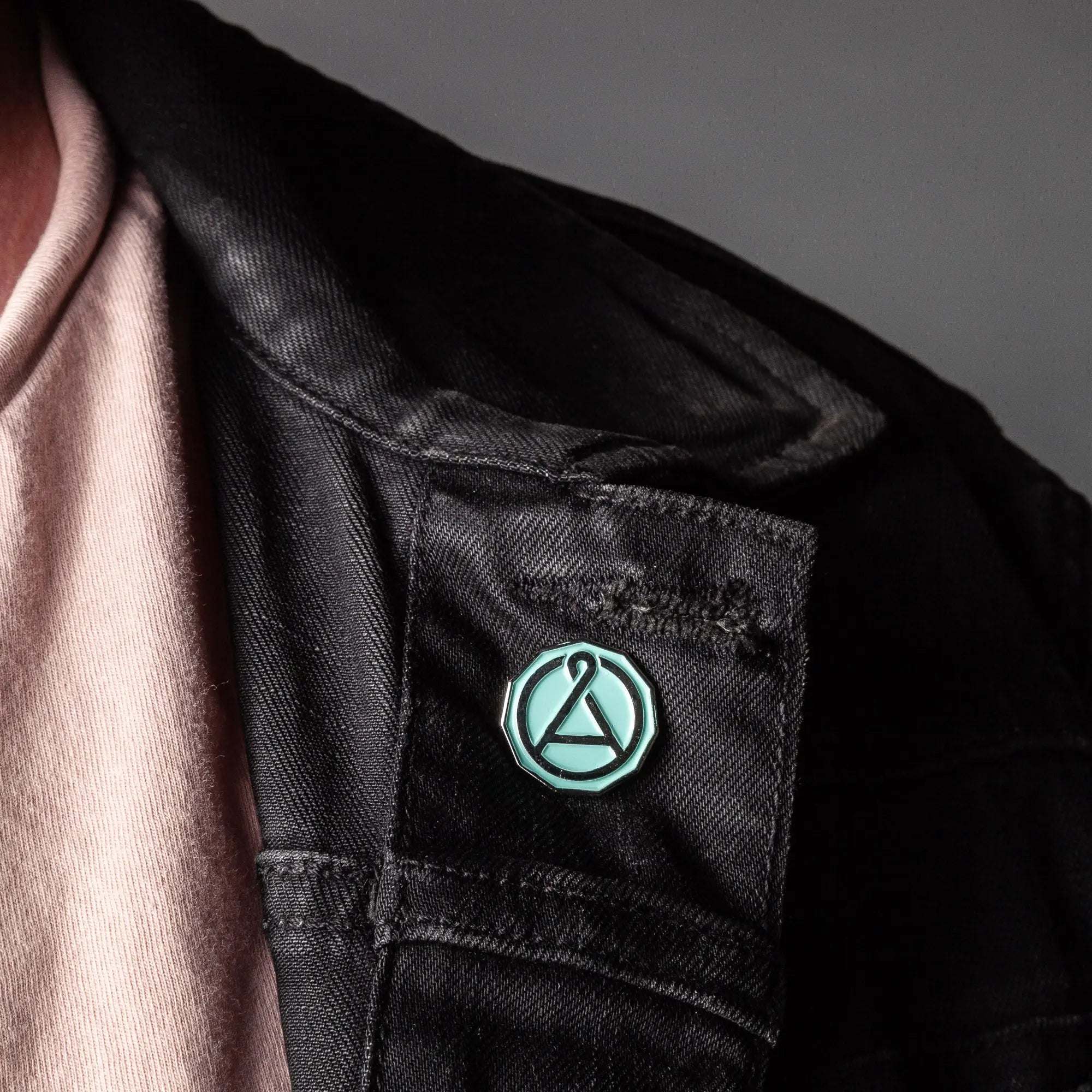 August Seal Enamel Pin in mint green and chrome, featuring a circular geometric seal design on a black jacket.