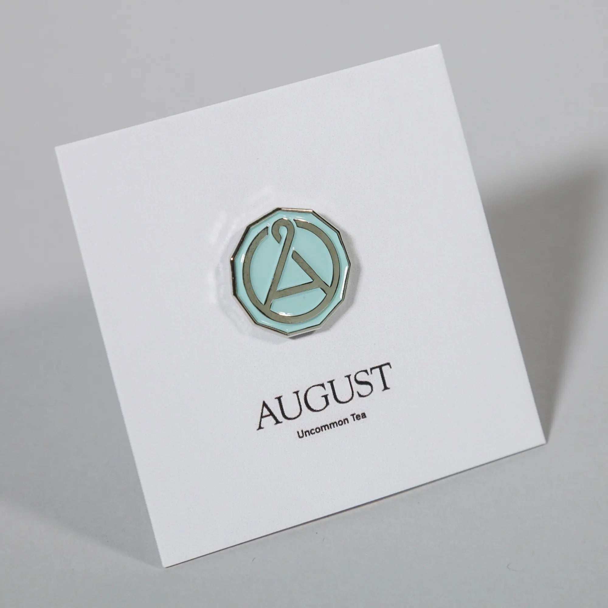 August Seal Enamel Pin with mint green enamel and chrome-tone metal edging, featuring a stylized seal emblem