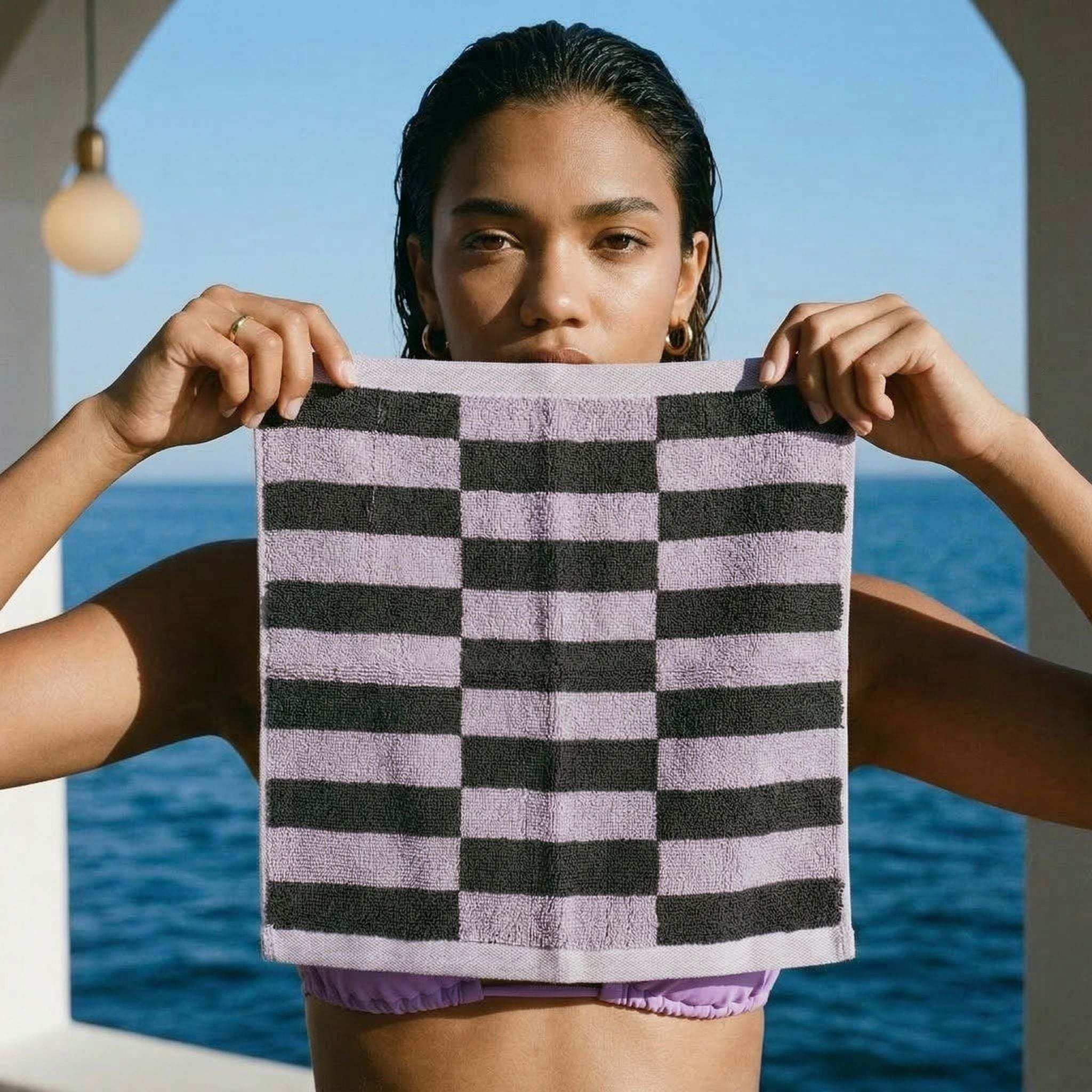 Australian Cotton towels featuring a geometric black and lilac checkered pattern in a soft, plush texture held by a person
