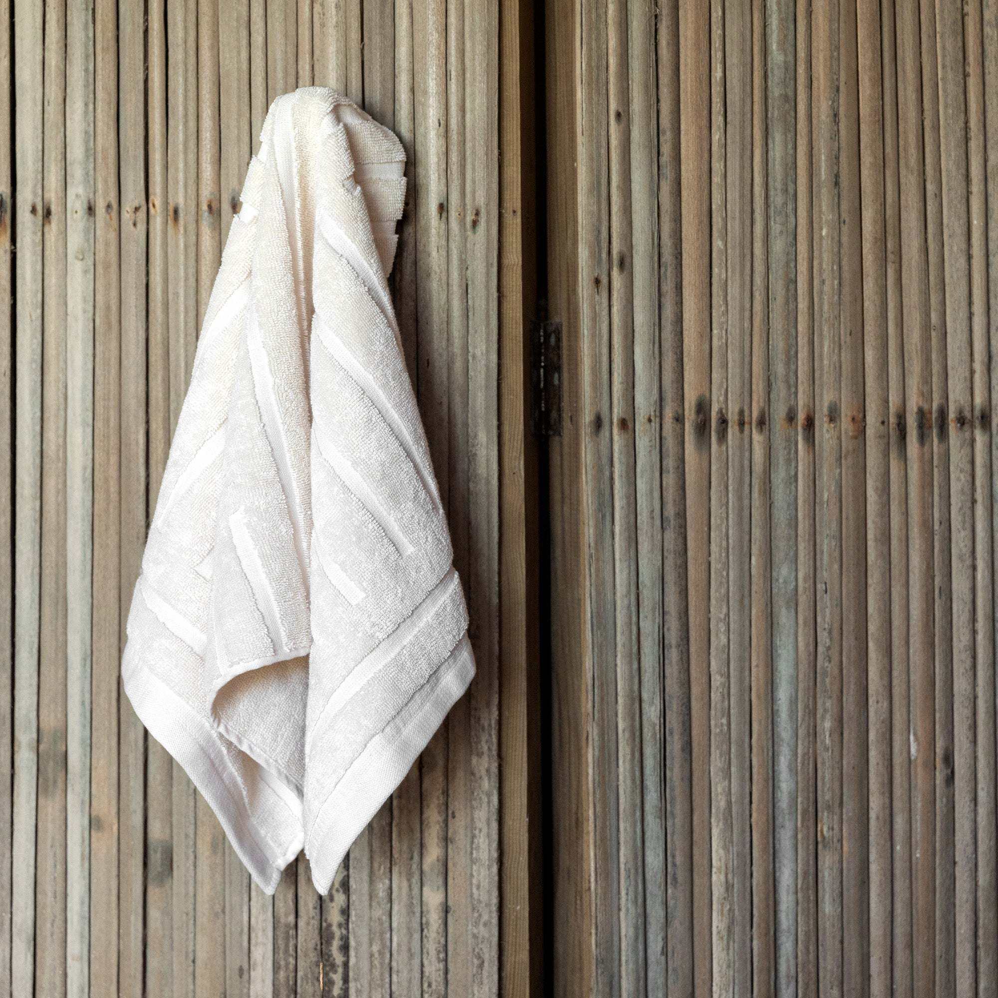 Australian Cotton towels in soft ecru color with a dense, plush texture and subtle geometric pattern hanging on a wooden rack