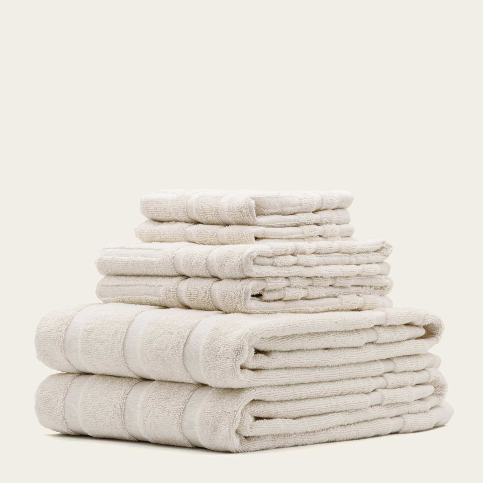 Stack of soft, plush ecru Australian Cotton towels with a subtle textured pattern and thick borders, showcasing premium quality.