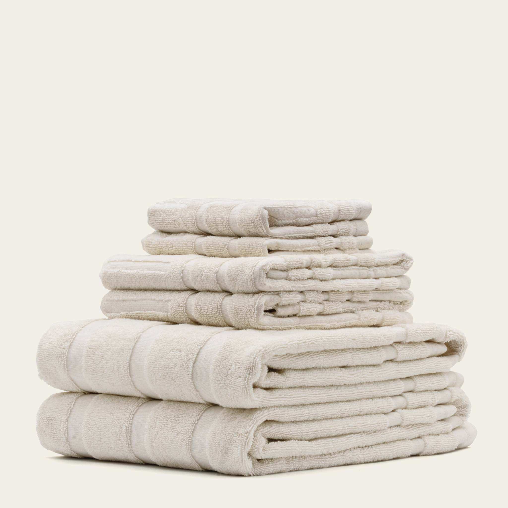Stack of ecru Australian Cotton towels including washcloths, hand towels, and bath towels with soft plush texture and subtle stripes