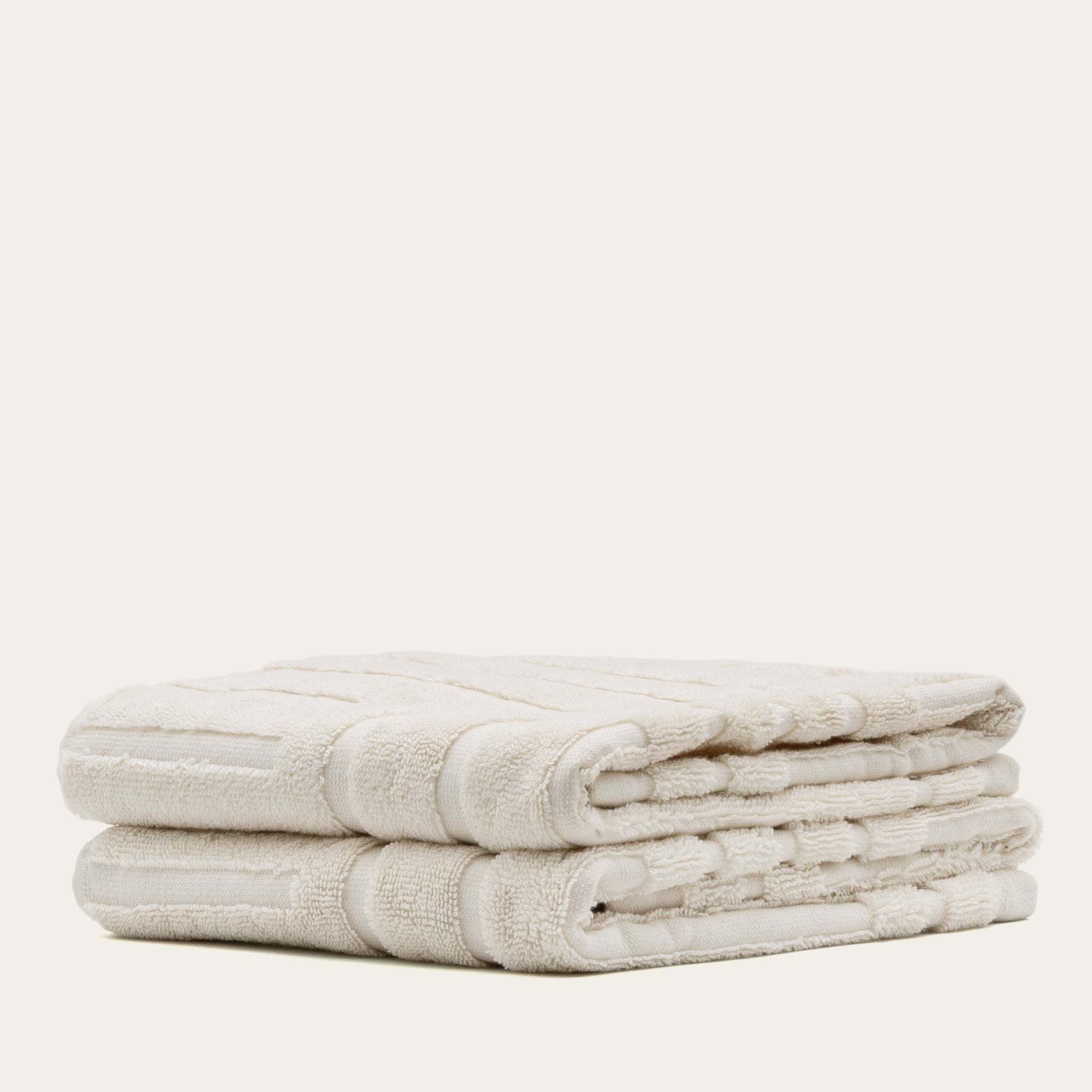 Set of soft ecru Australian Cotton towels with a subtle geometric pattern, plush and dense weave, folded neatly