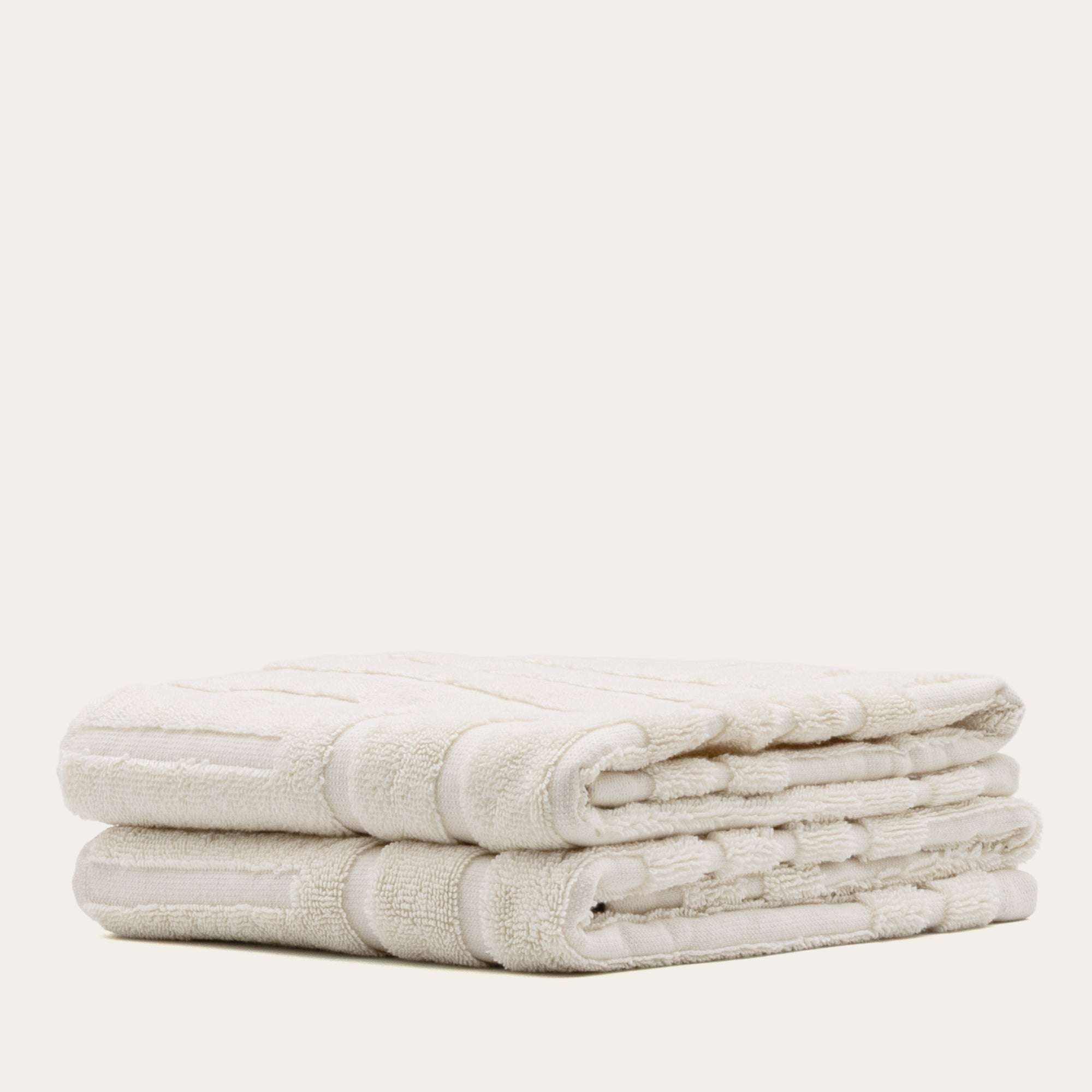 Set of folded ecru Australian Cotton towels with a subtle geometric pattern, featuring plush 600 GSM cotton texture