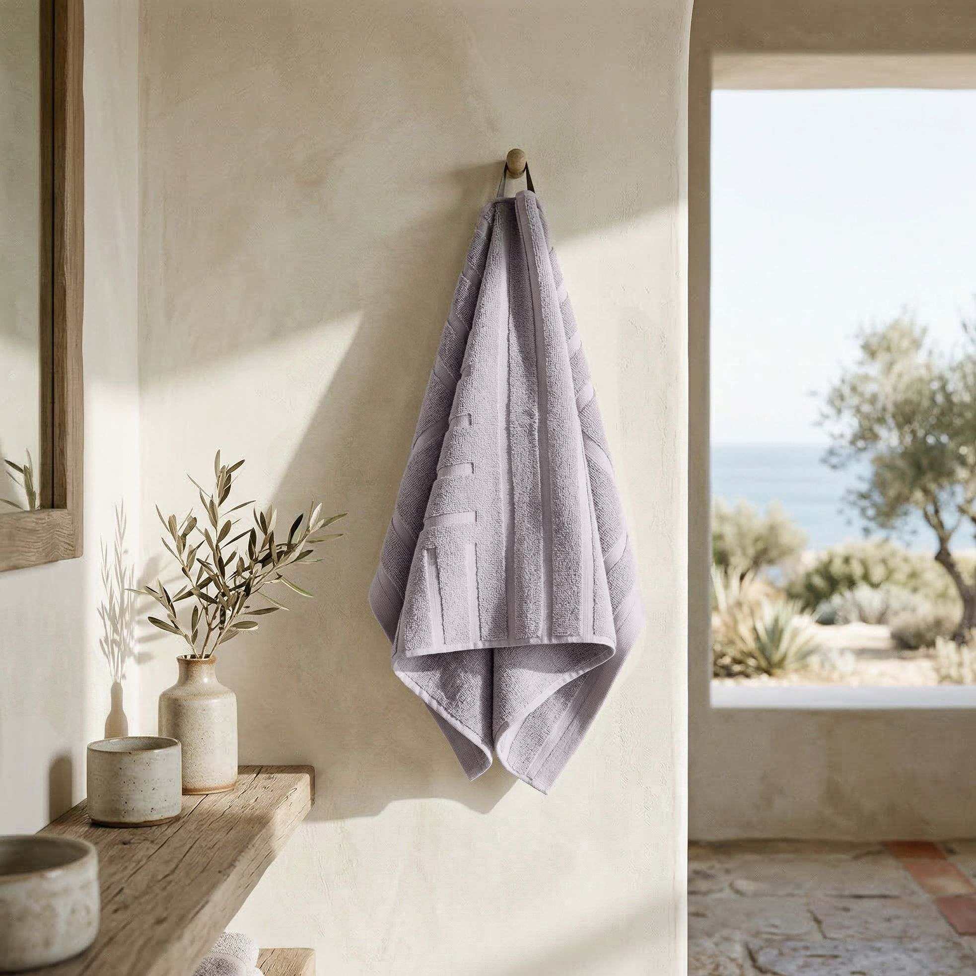 Australian Cotton towels in soft lilac with subtle geometric pattern hanging on wooden peg, plush and absorbent texture