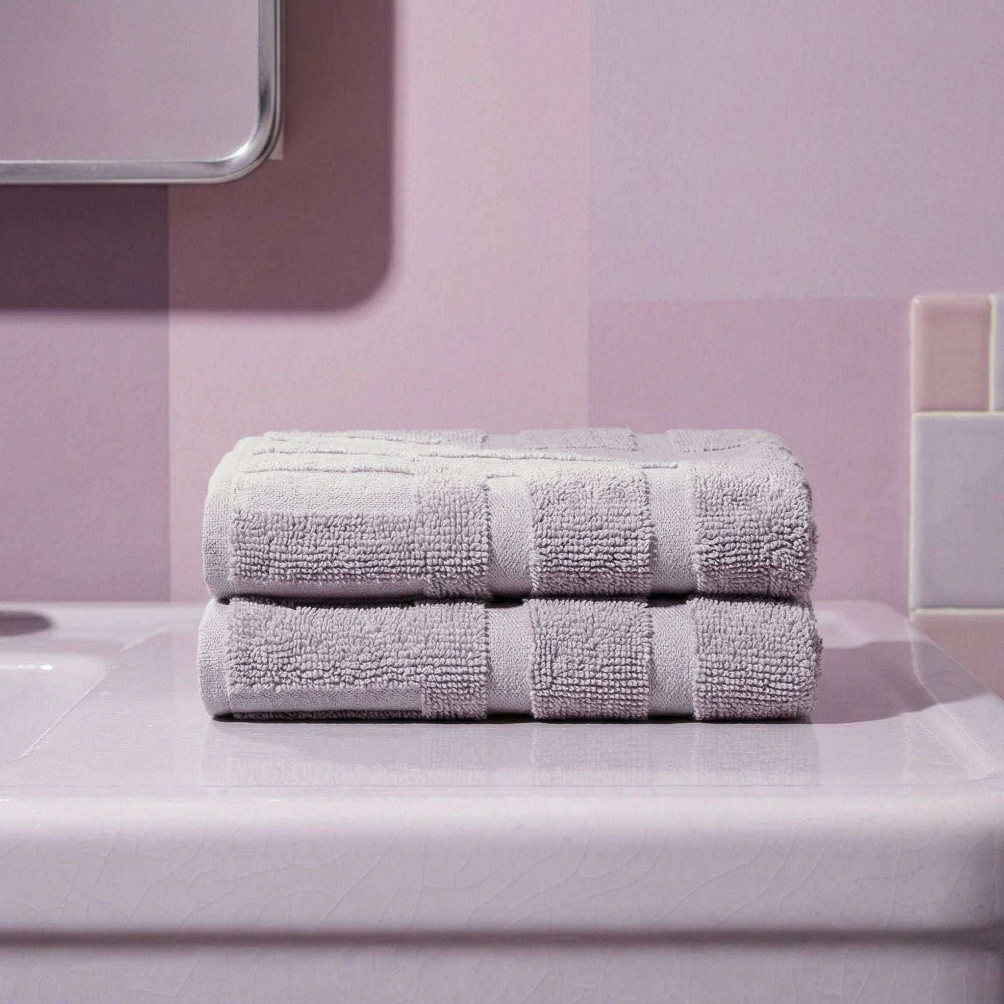 Australian Cotton towels in soft lilac with geometric pattern, dense plush texture and neat edges stacked on a beige surface