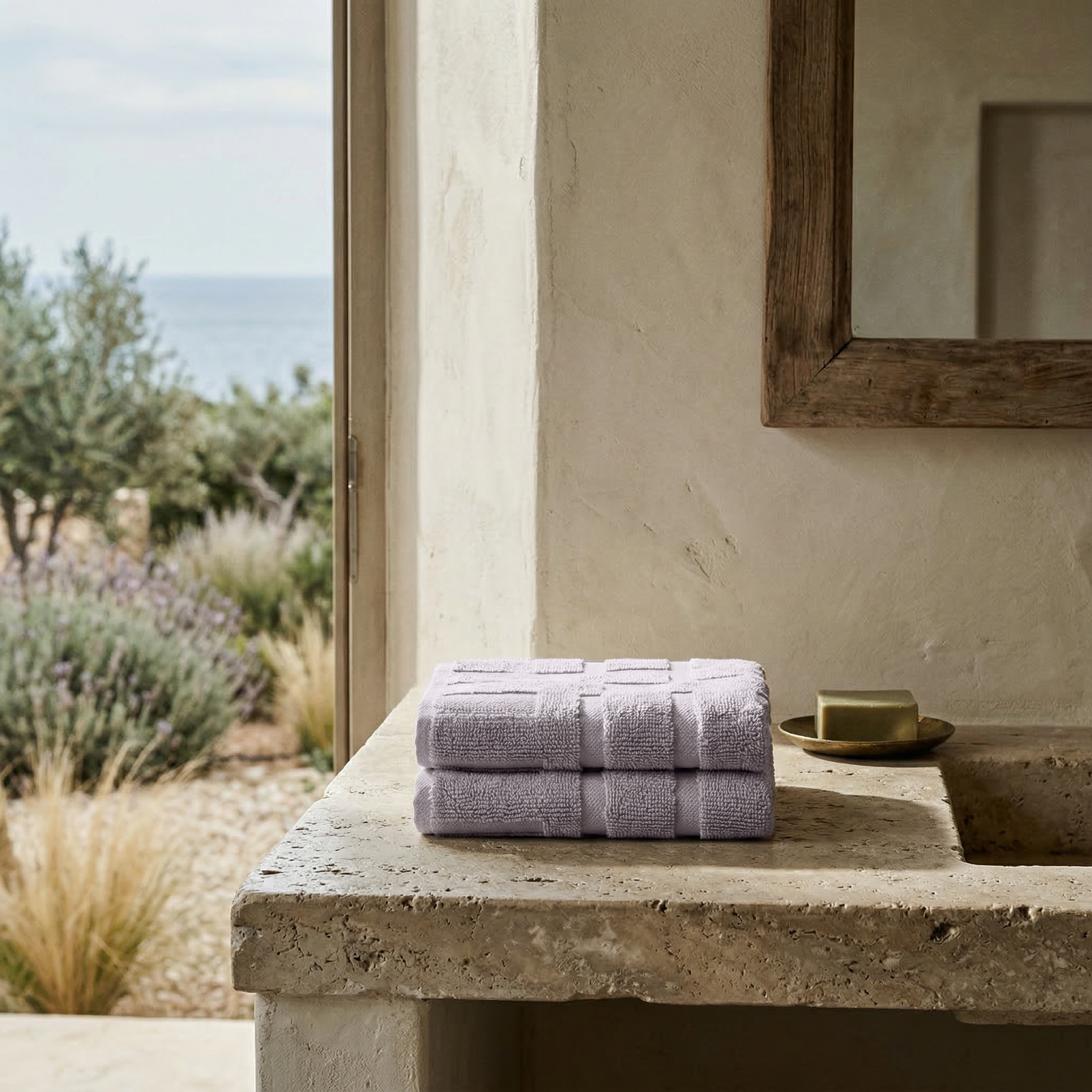 Lilac Australian Cotton towels with geometric patterns folded on a stone countertop beside a soap dish in a neutral bathroom setting