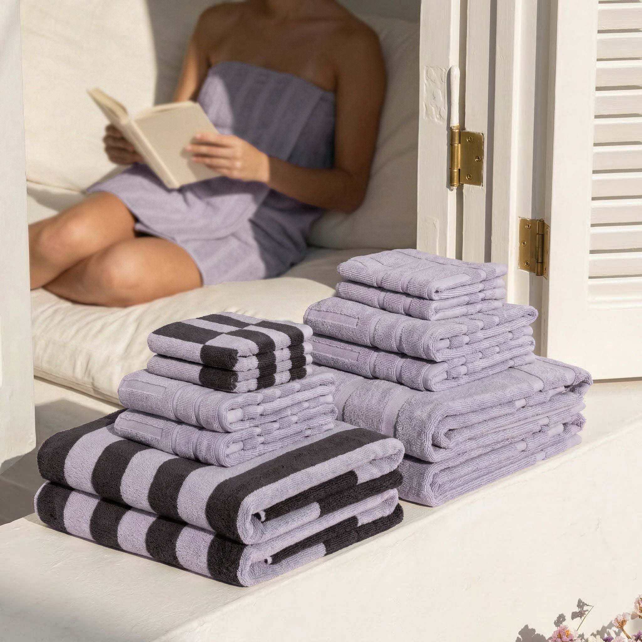 Australian Cotton towels in lilac with geometric black stripe patterns, stacked in various sizes next to a person wrapped in a lilac towel