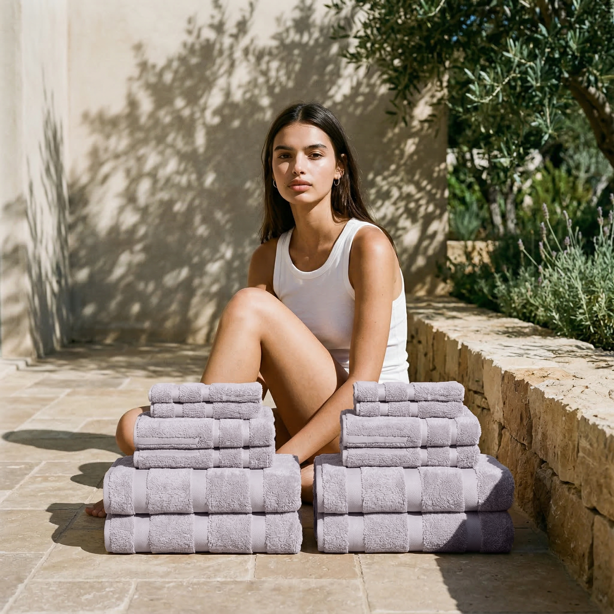 Stacked lilac Australian Cotton towels in various sizes with a smooth texture, presented alongside a woman in a white tank top