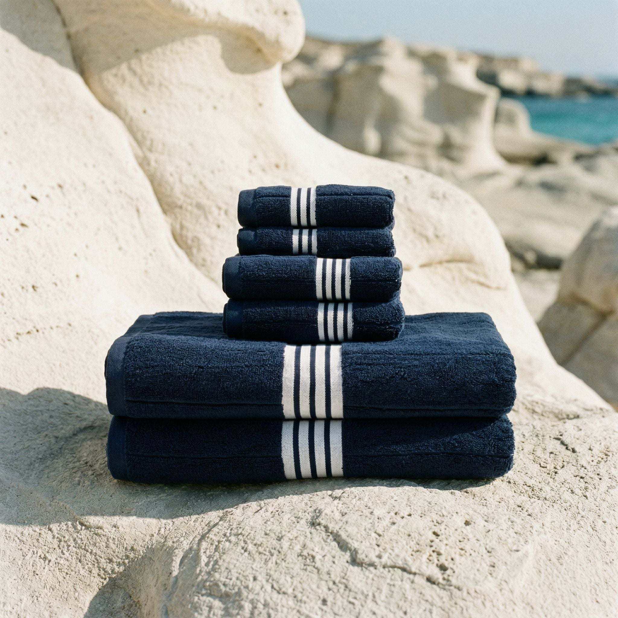 Australian Cotton towels in navy blue featuring a dense soft cotton texture with white triple stripe accents stacked on a natural rock surface