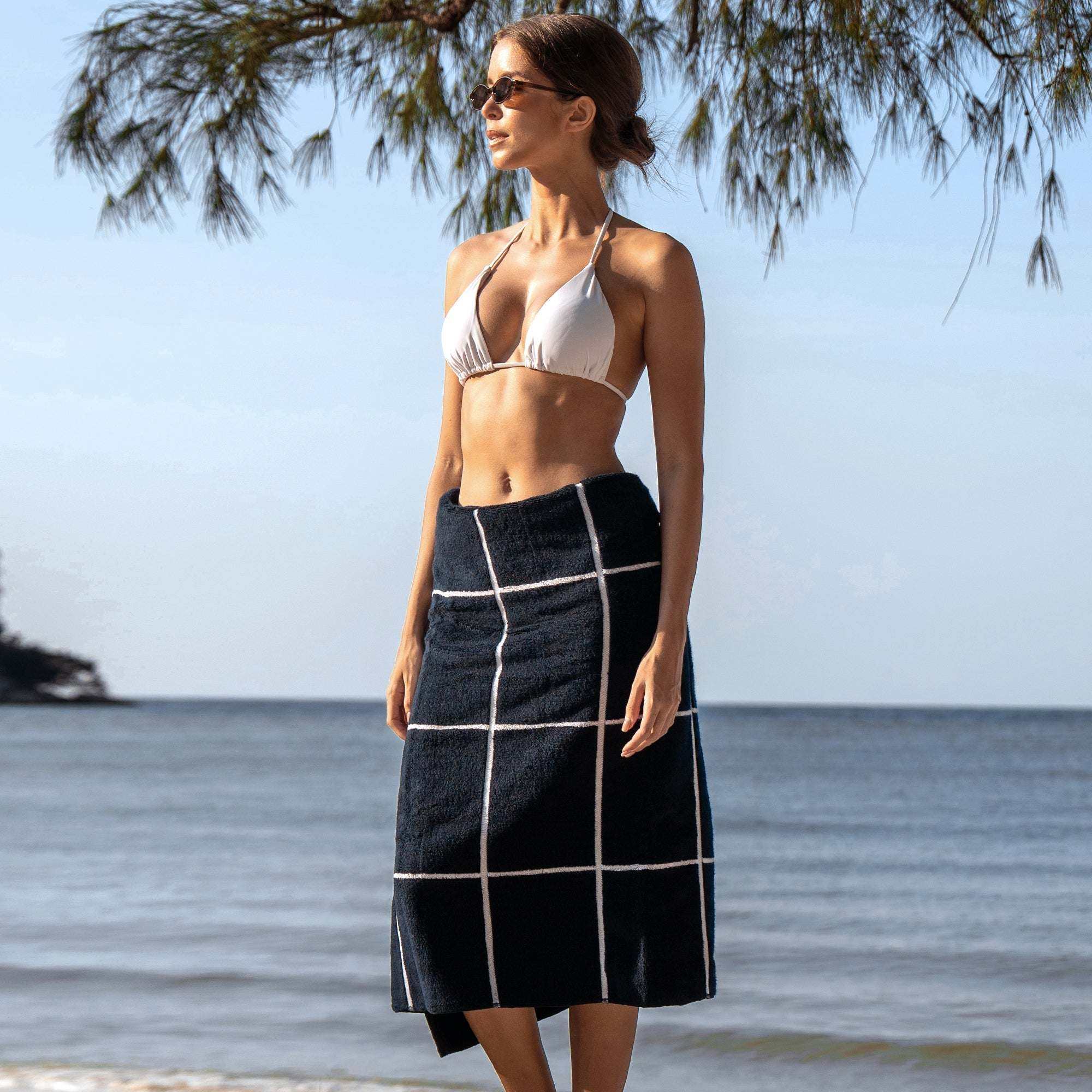 Australian Cotton towels in navy with white geometric grid pattern worn as a wrap skirt by a woman at the beach