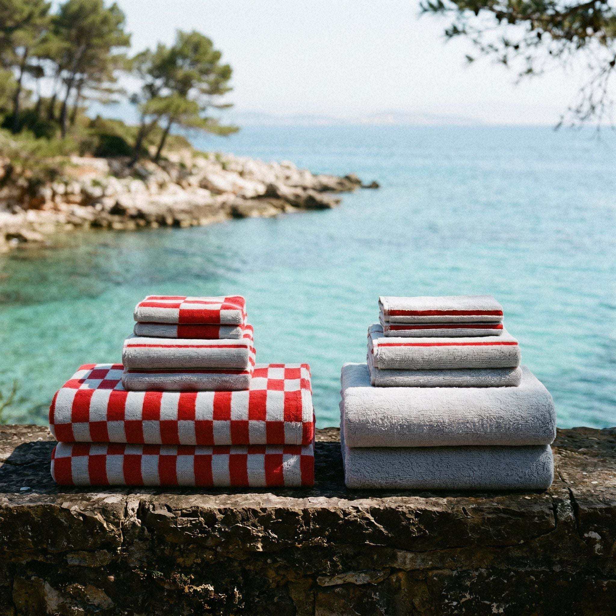 Australian Cotton towels set featuring red and white checkered pattern and solid light grey towels arranged by the water