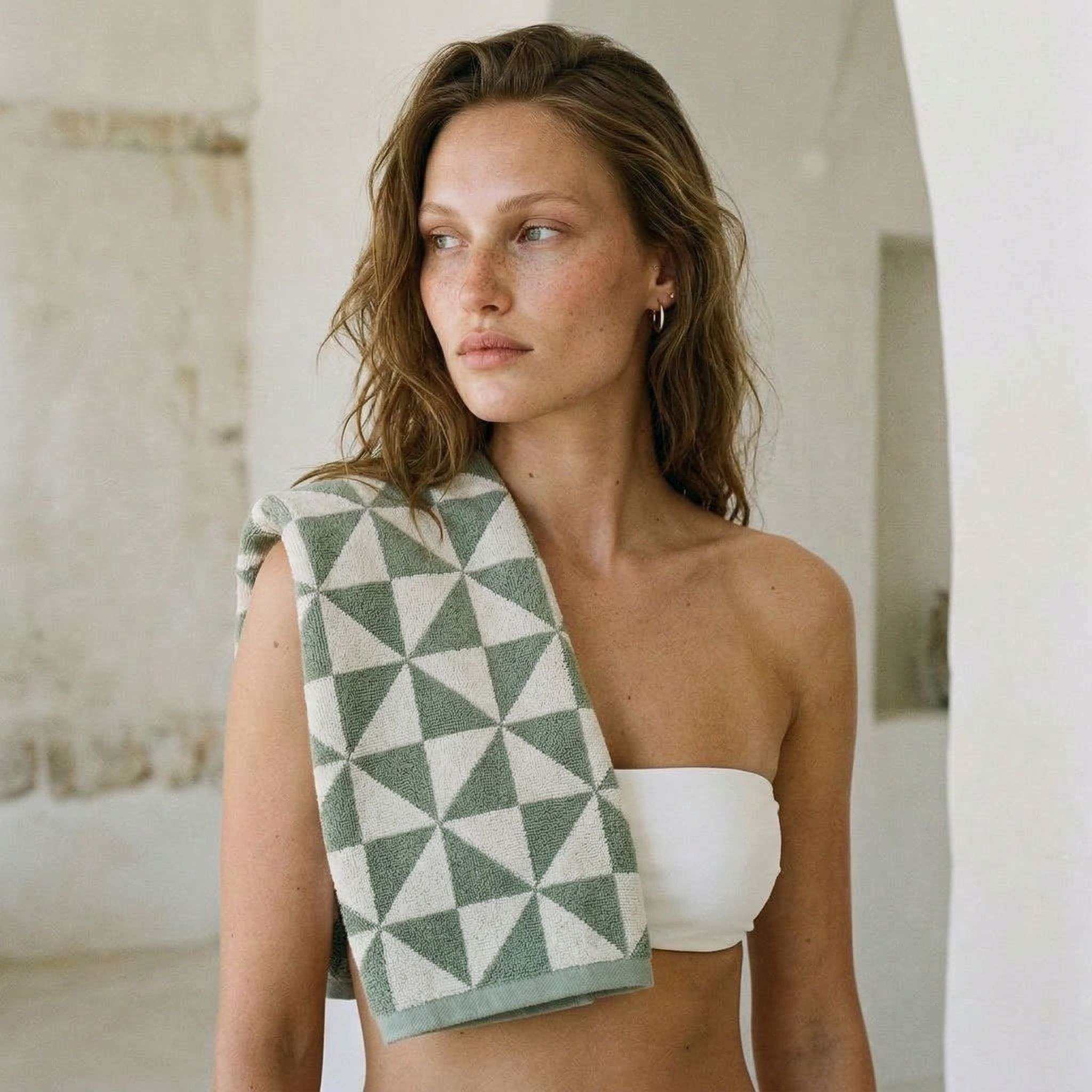 Australian Cotton towels with sage and ecru geometric pattern draped over shoulder of woman wearing white bandeau top