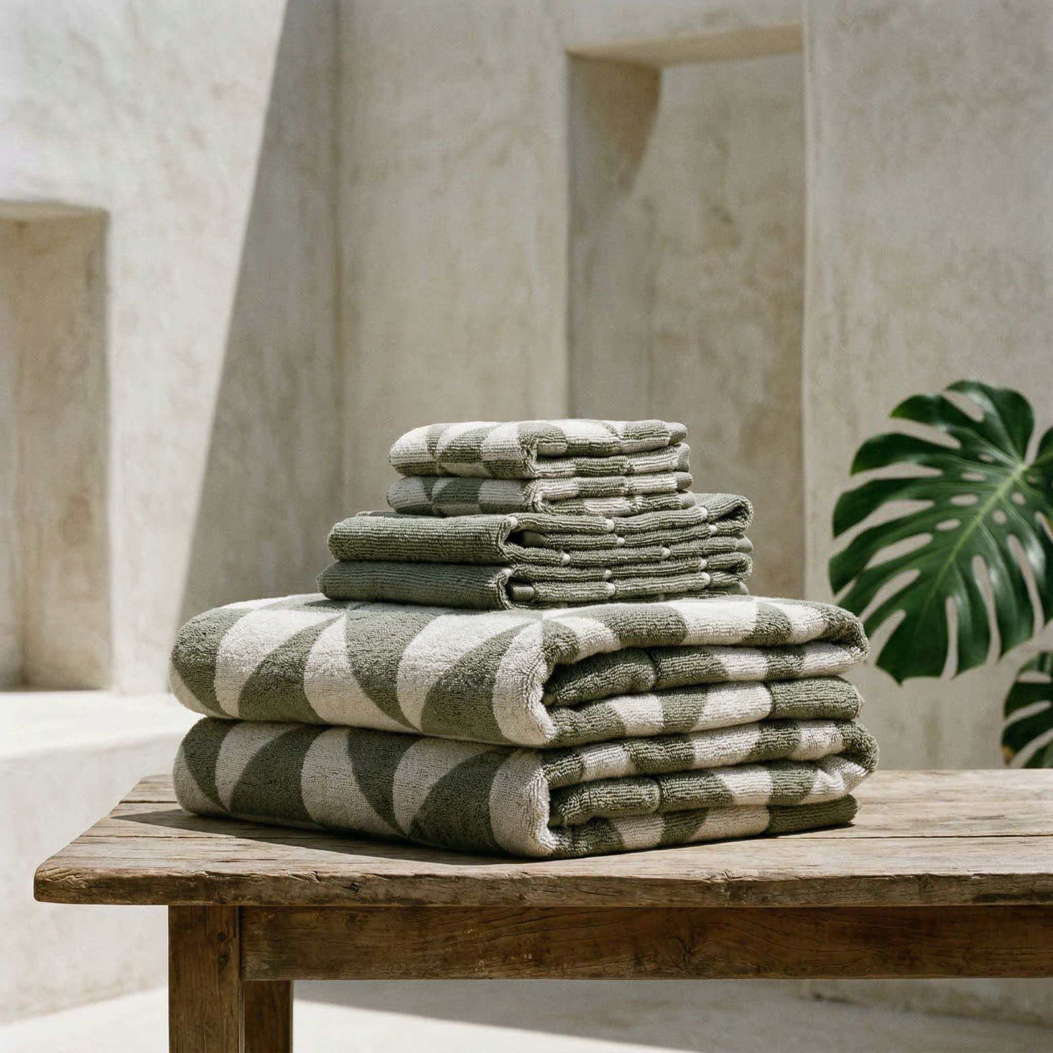 Australian Cotton towels in sage green with white geometric patterns, made of plush, dense cotton, folded on wooden surface