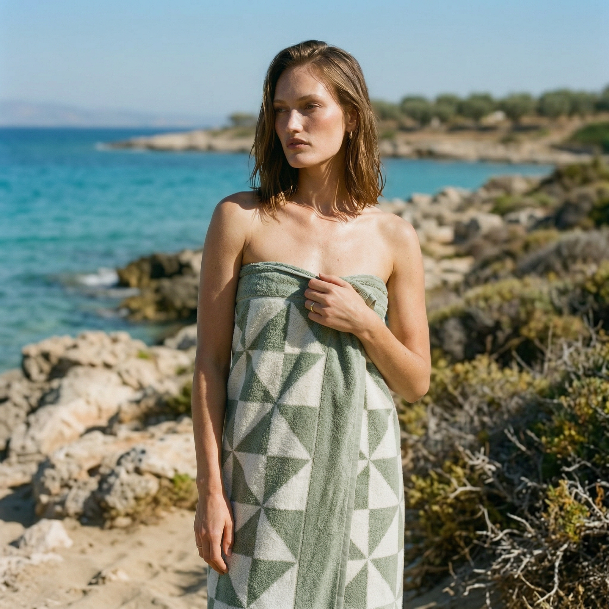 Australian Cotton towels in sage with contemporary geometric patterns wrapped around a woman standing by the rocky beach