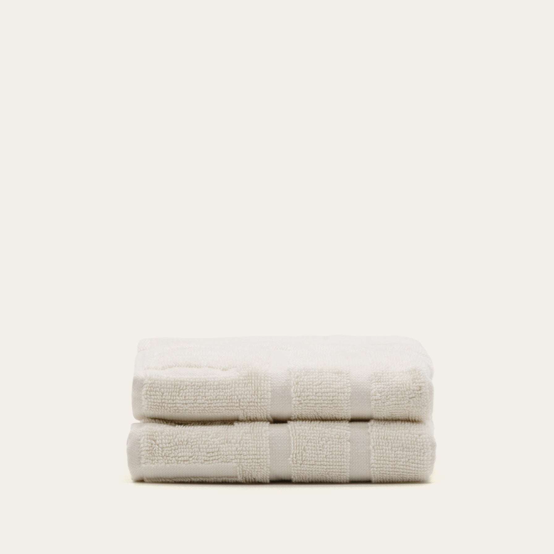 Stack of two soft ecru Australian Cotton towels featuring a geometric pattern and plush texture