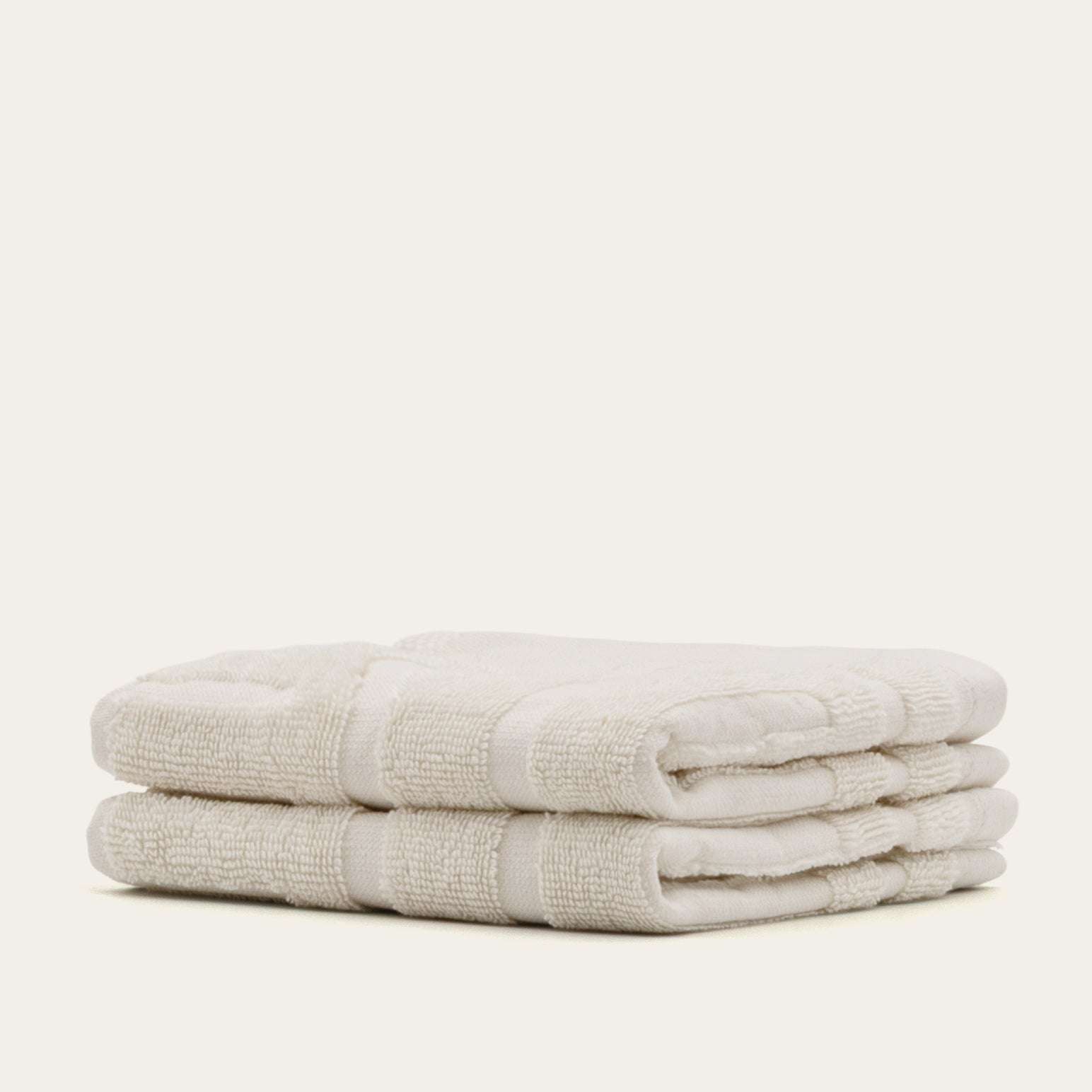 Stack of soft ecru Australian Cotton towels with a dense texture and subtle striped pattern