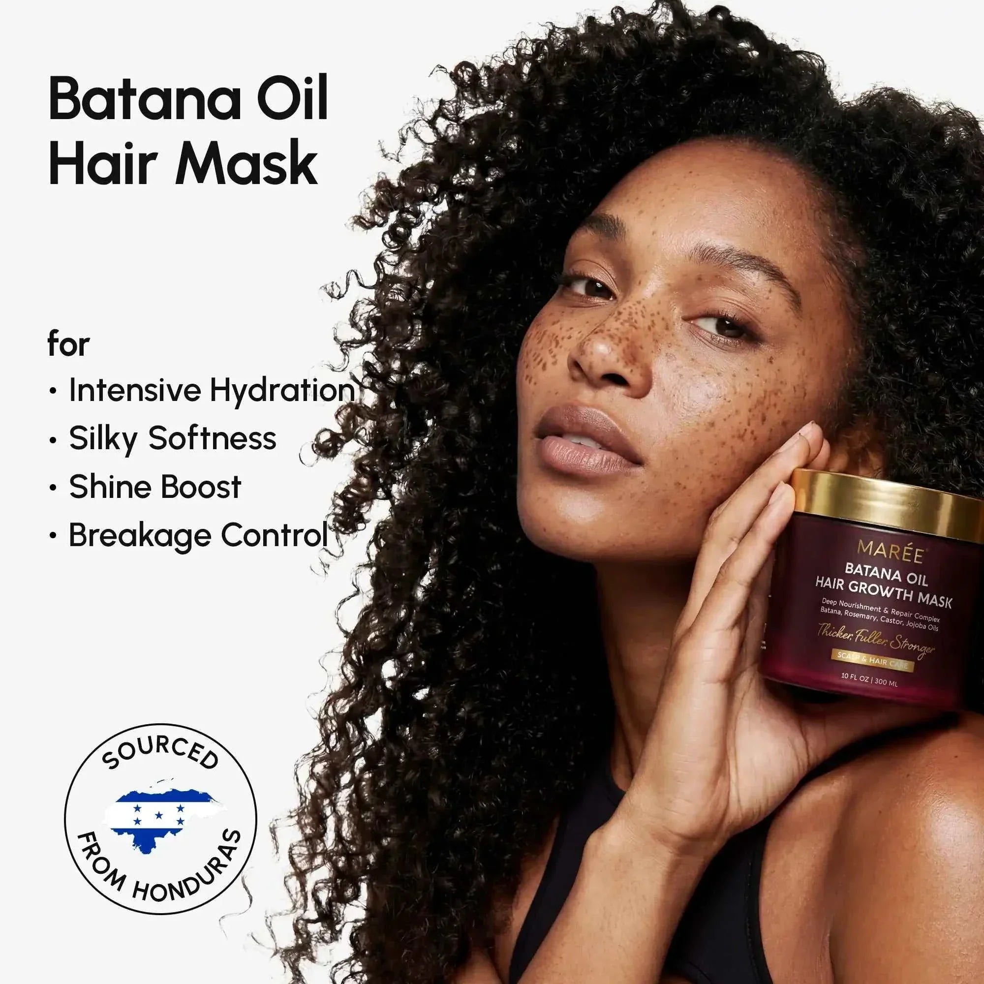 Batana Hair Growth Mask in a deep burgundy jar with a gold lid, held beside a model’s natural curly hair