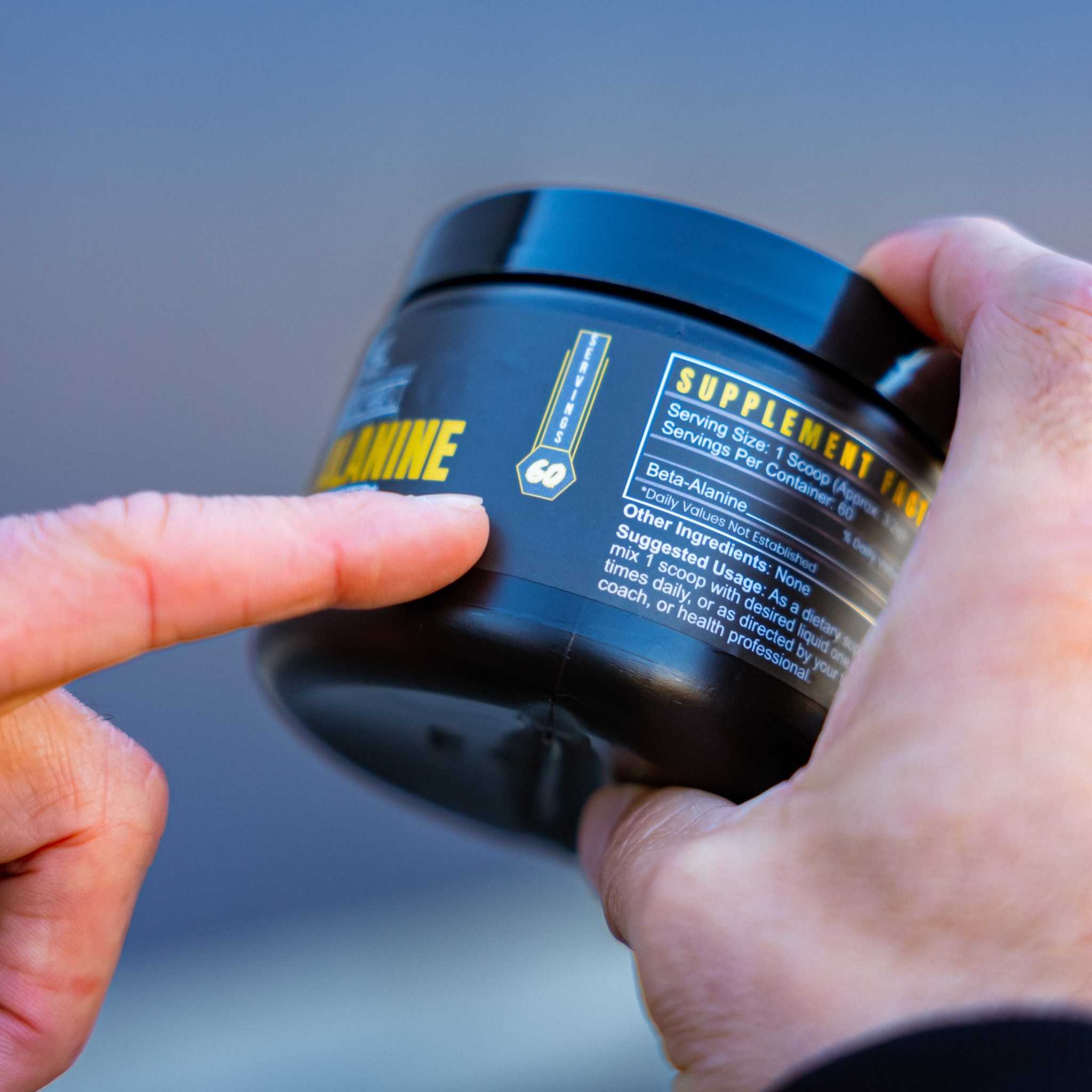 BETA-ALANINE supplement in a black tub with blue labeling and yellow lettering, held in hands
