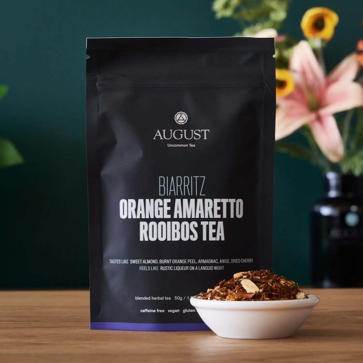 Biarritz - Orange Amaretto Rooibos Tea in a black pouch with rooibos tea and almond pieces in a white bowl