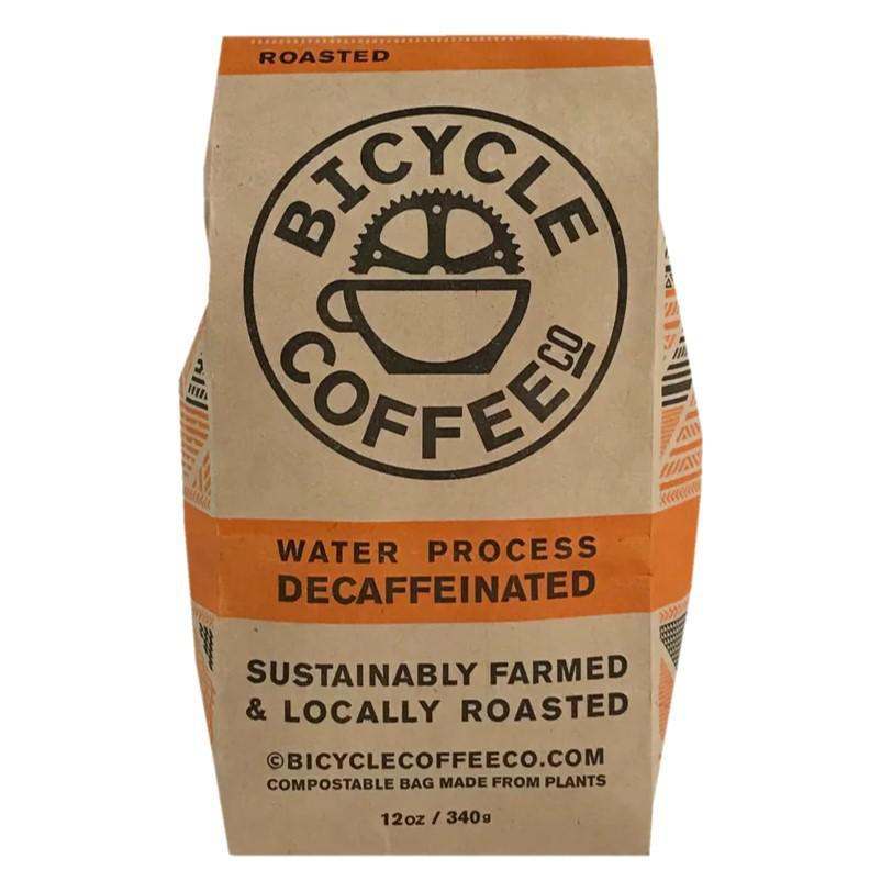 Bicycle decaf Coffee in a brown kraft paper bag with orange accents, featuring water process decaffeinated labeling and sustainable roasting claims