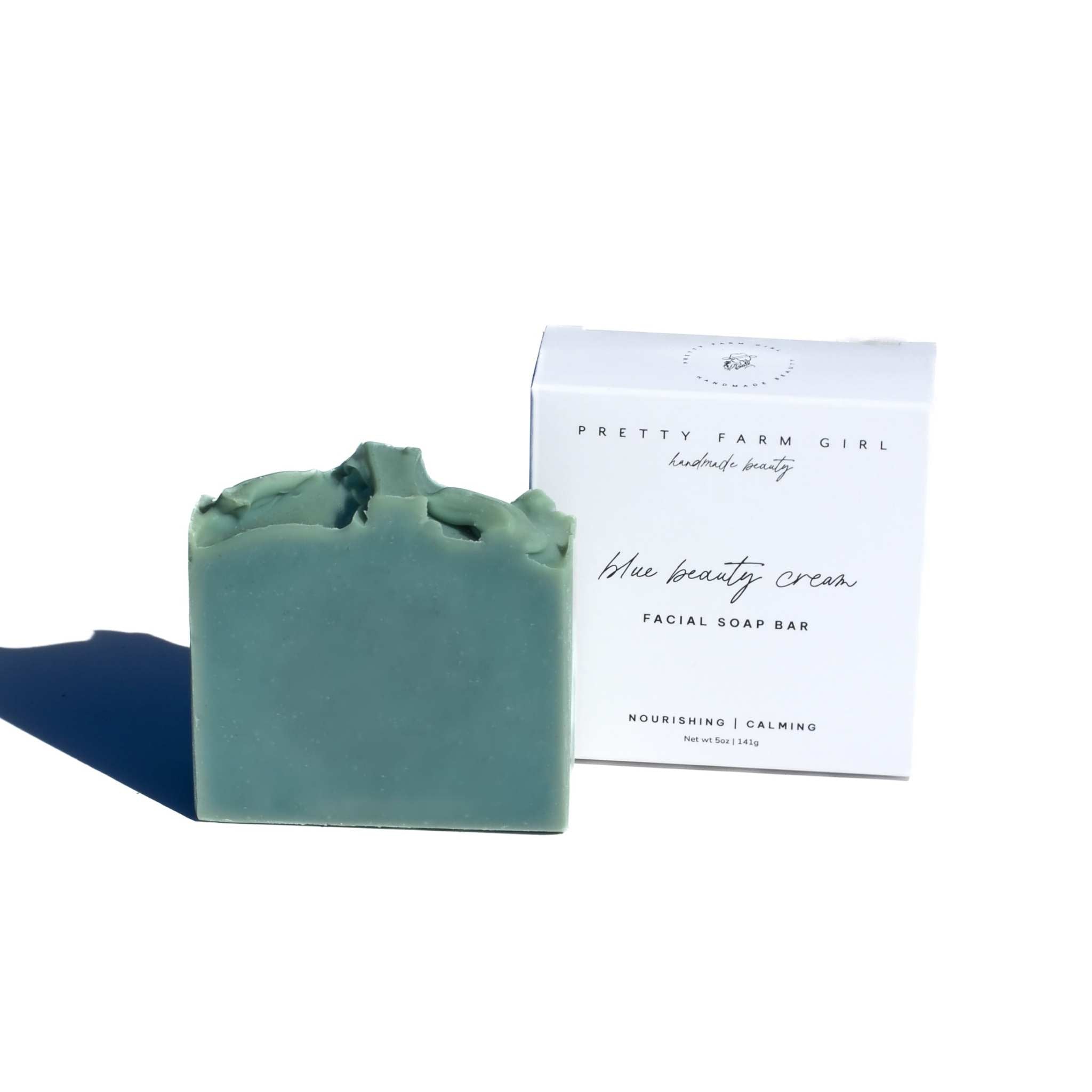 Blue Beauty Cream Facial Bar, blue-green handmade soap with a textured top beside its white box packaging