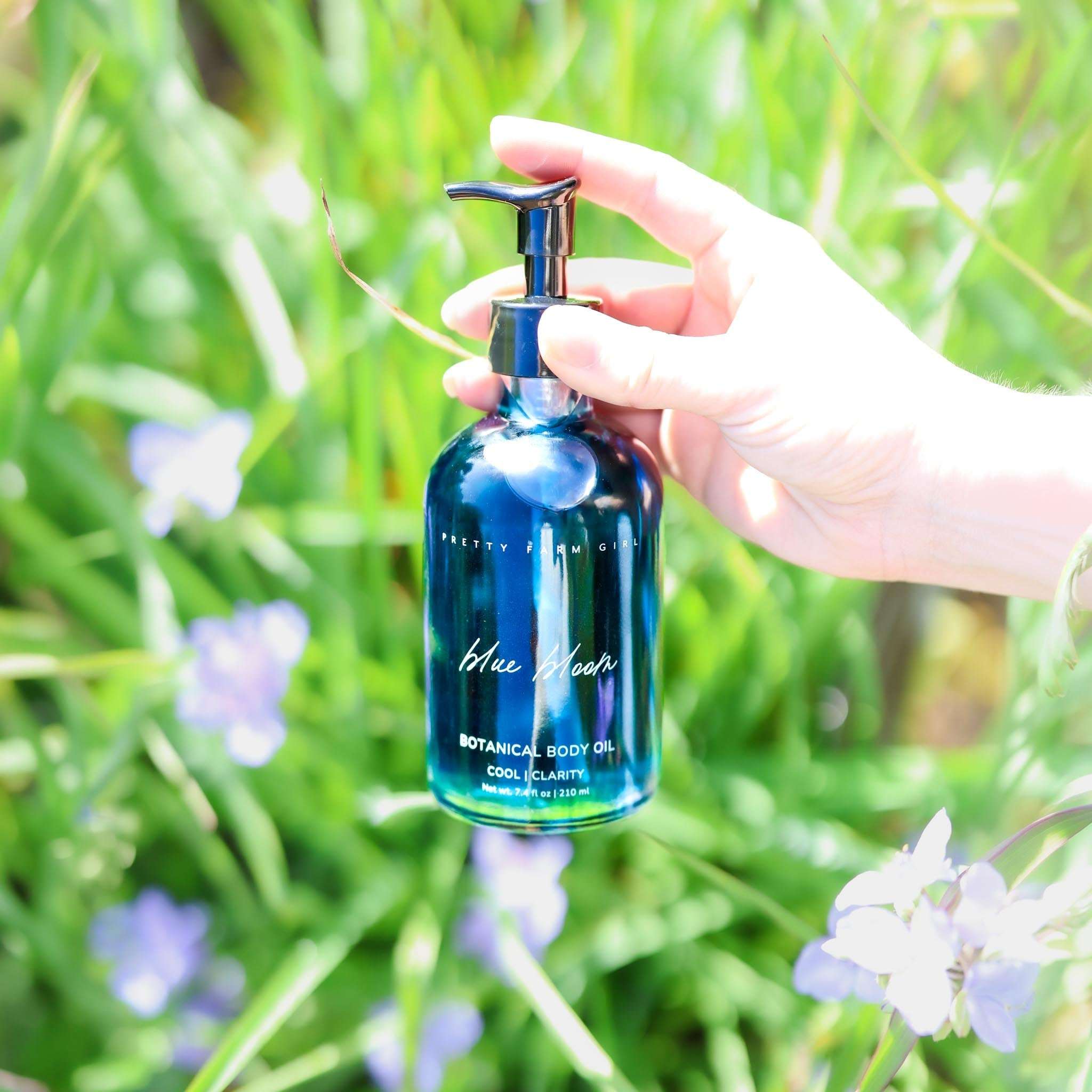Blue Bloom Botanical Body Oil in a deep blue glass pump bottle, featuring white botanical lettering and a silver dispenser