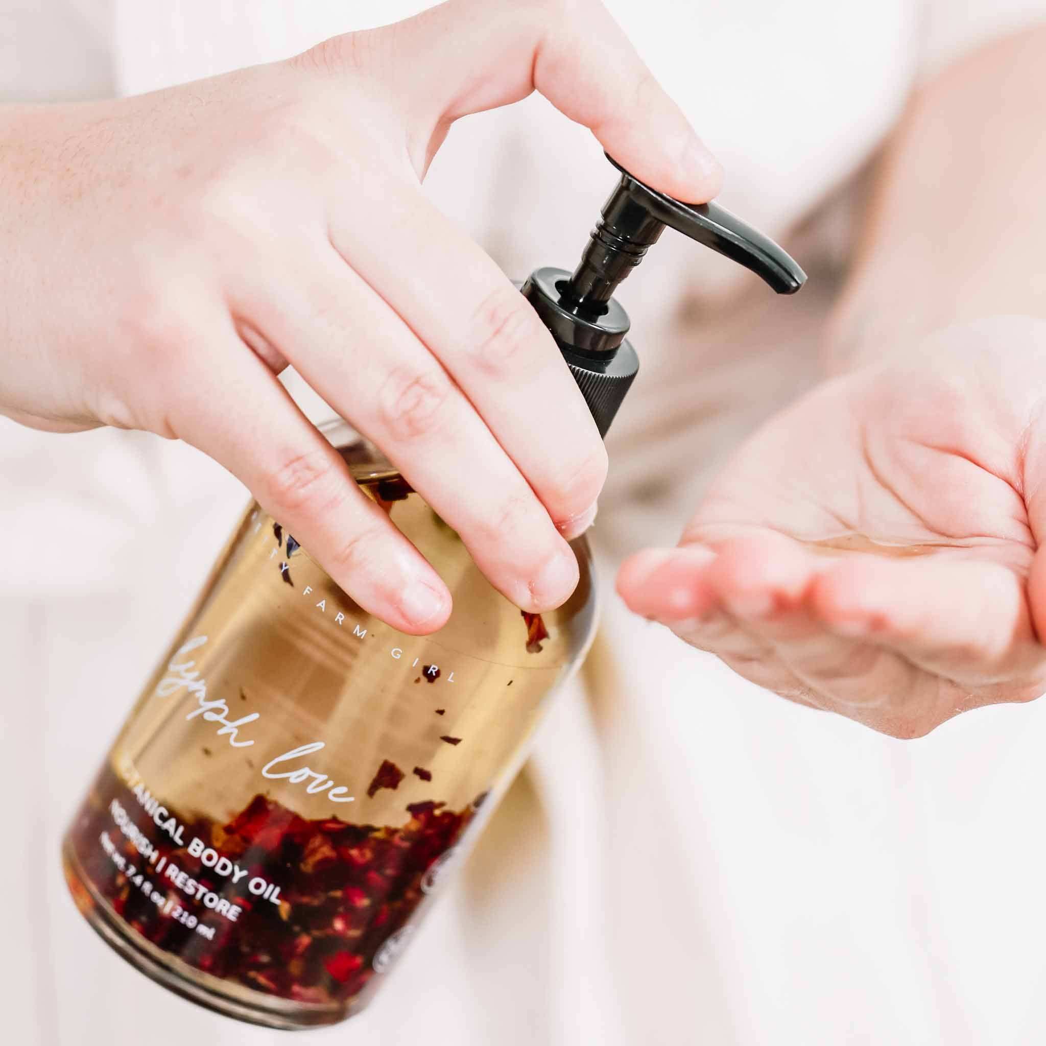 Body Care Lymphatic Routine Kit featuring amber glass body oil bottle with black pump and botanical petals visibly suspended inside