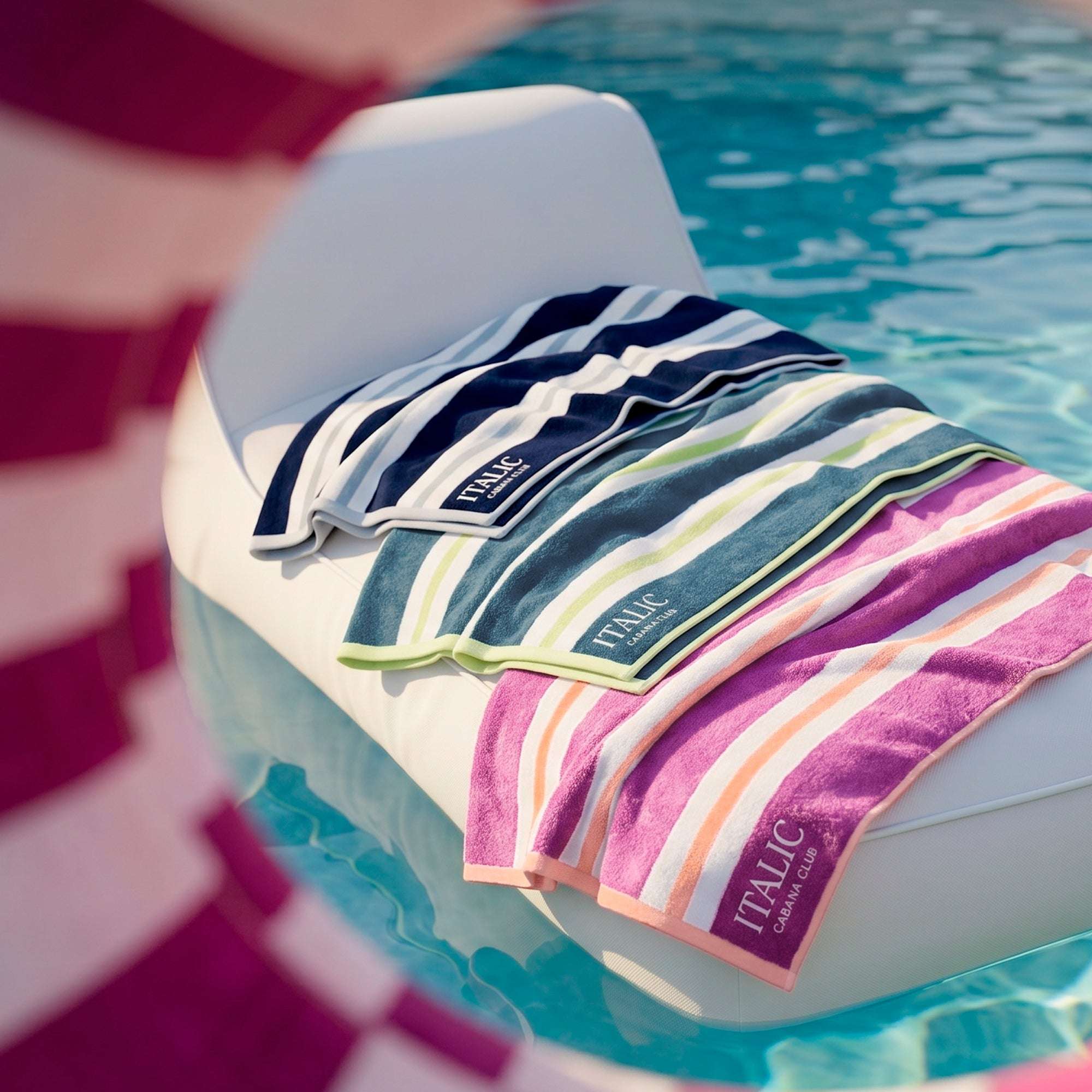 Bondi Australian Cotton beach towels in navy, teal and pink striped cotton, draped over a poolside chair