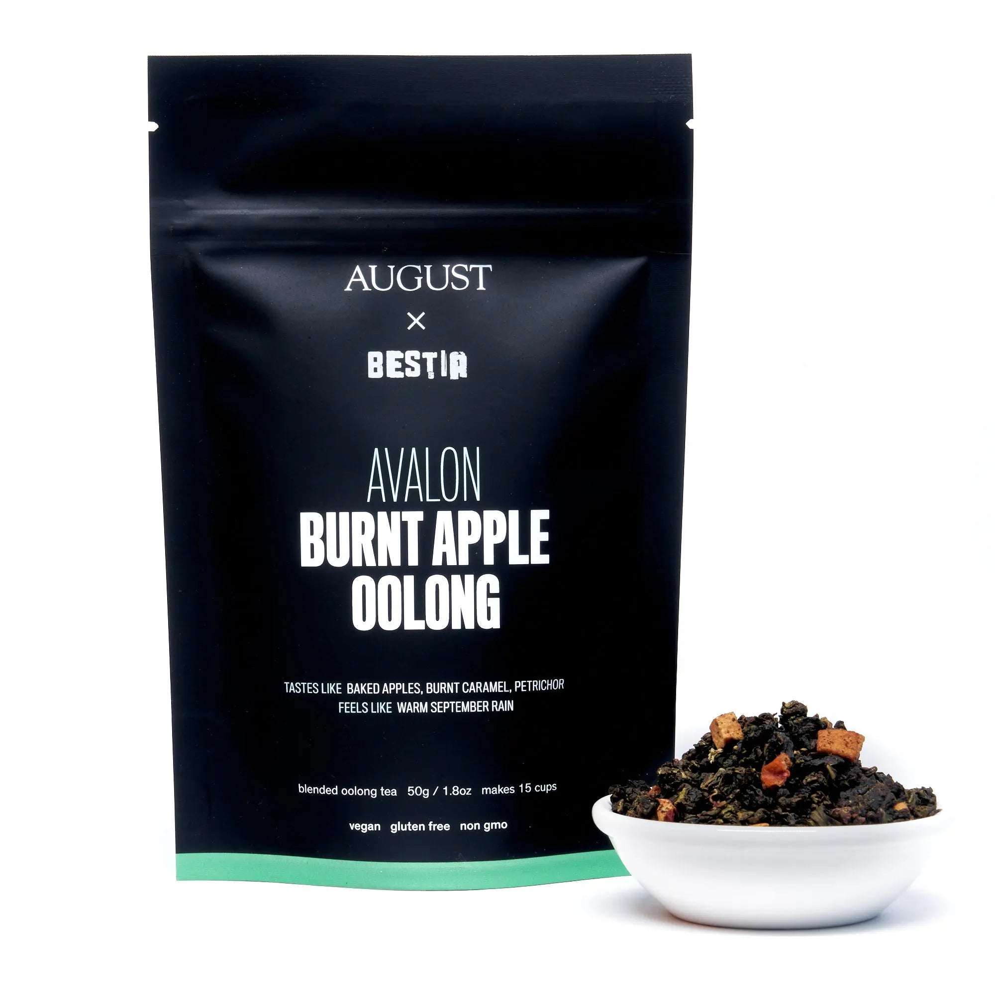 Burnt Apple Oolong Tea in a black Avalon pouch with white lettering, shown beside loose dark tea and apple pieces