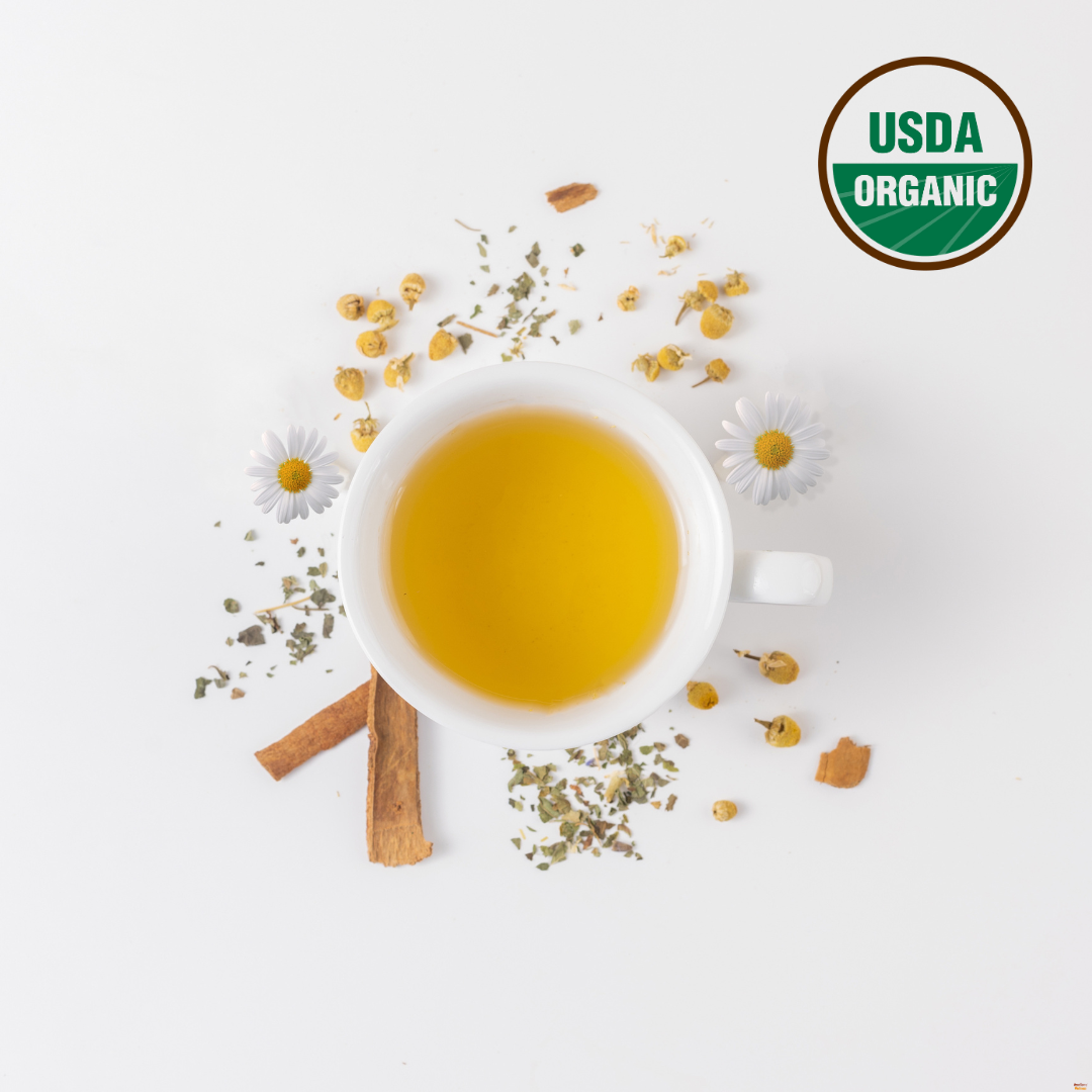 Calm-In-A-Teacup organic chamomile tea in white cup with cinnamon sticks, chamomile flowers, and dried herbs on white background