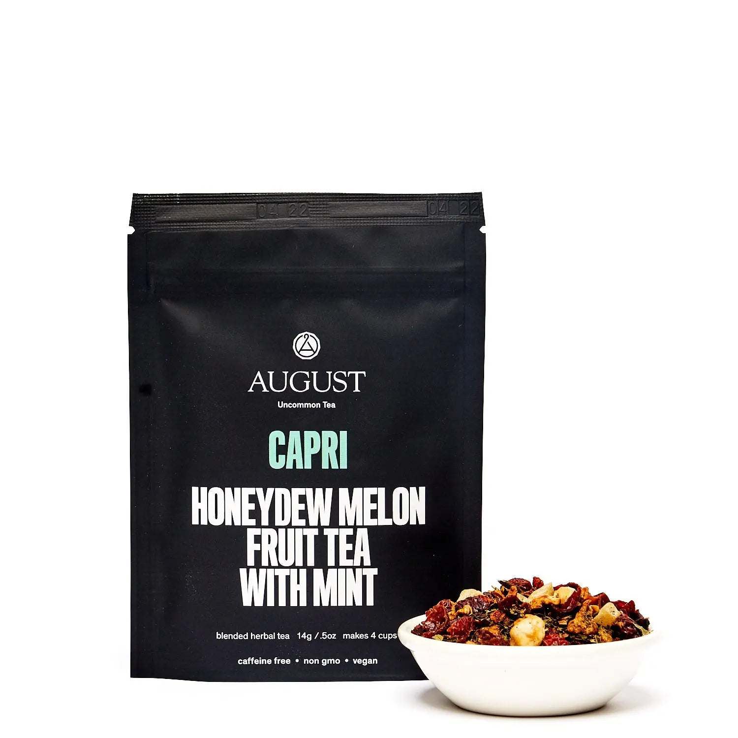 Capri - Honeydew Melon Mint Tea in a matte black pouch beside a bowl of colorful dried fruit and mint tea