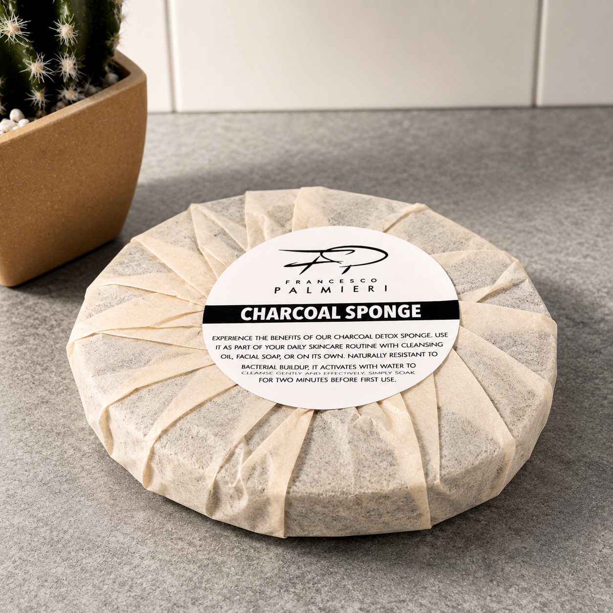 Charcoal Infused Face Sponge with a beige porous texture, wrapped in a cream paper band with a black label