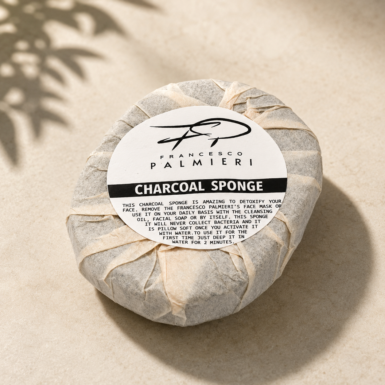 Charcoal Infused Face Sponge wrapped in cream paper, with a round charcoal sponge and bold black label