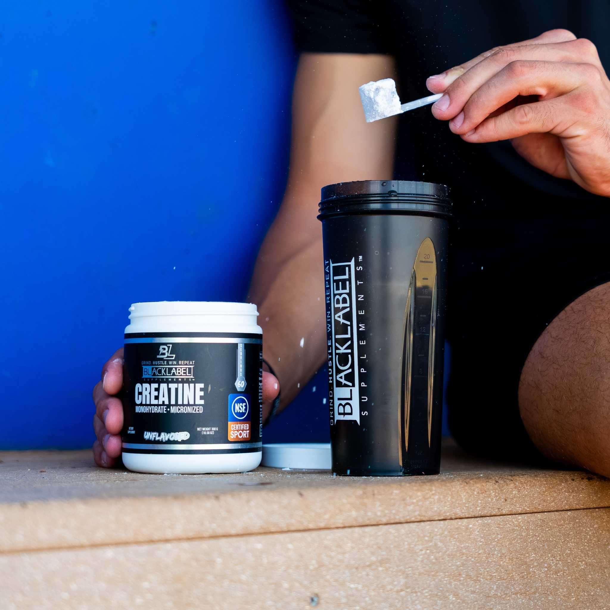 CREATINE MONOHYDRATE supplement in a white tub beside a black shaker, with a scoop of white powder