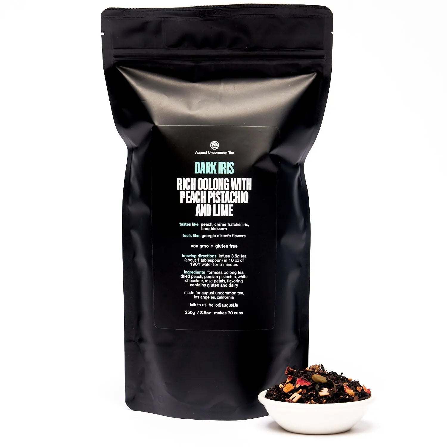 Dark Iris - Peach Pistachio Oolong Tea in a matte black pouch with a white bowl of loose tea leaves