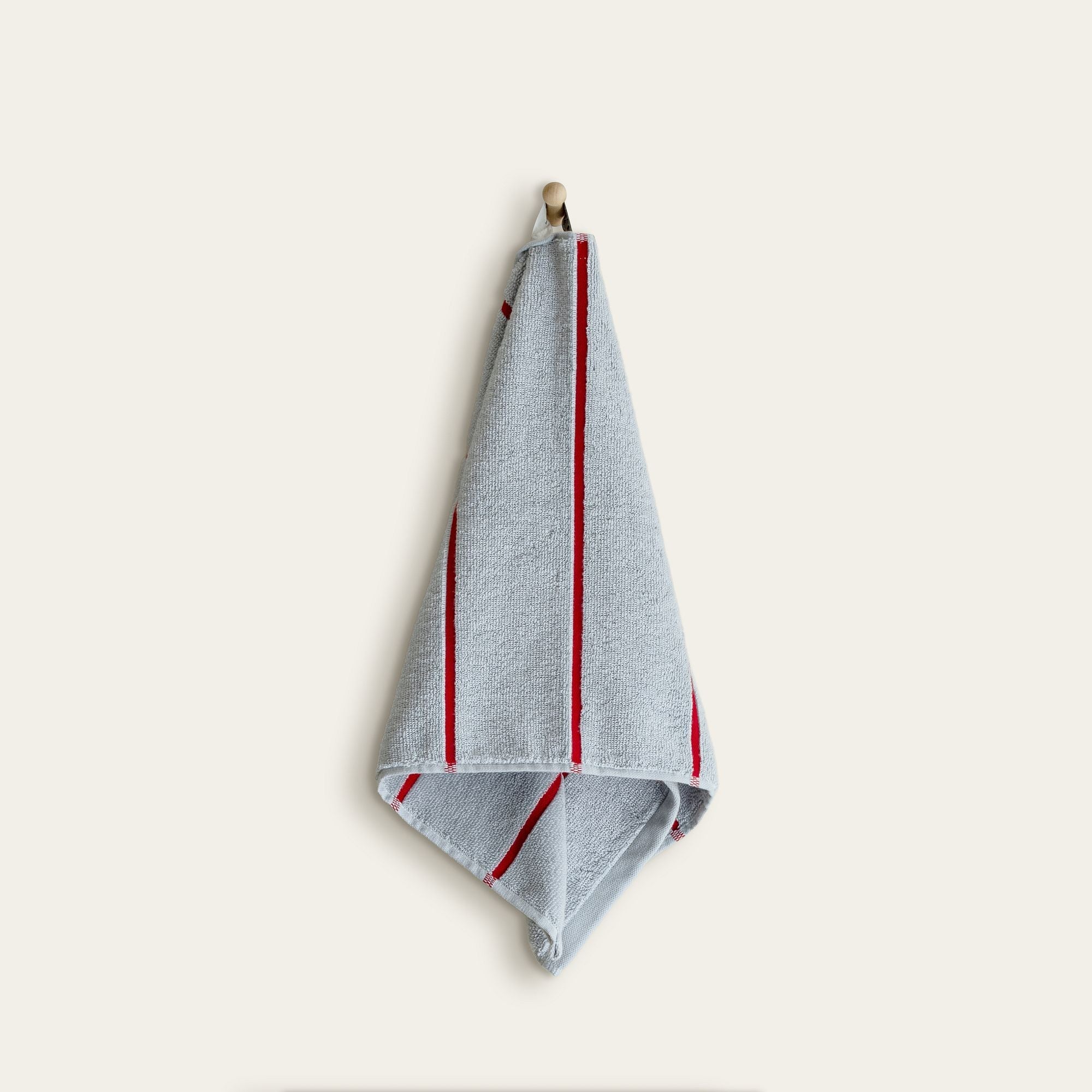 Deia Australian Cotton towel in light gray, showing a plush terry texture and narrow red stripes along the edges.