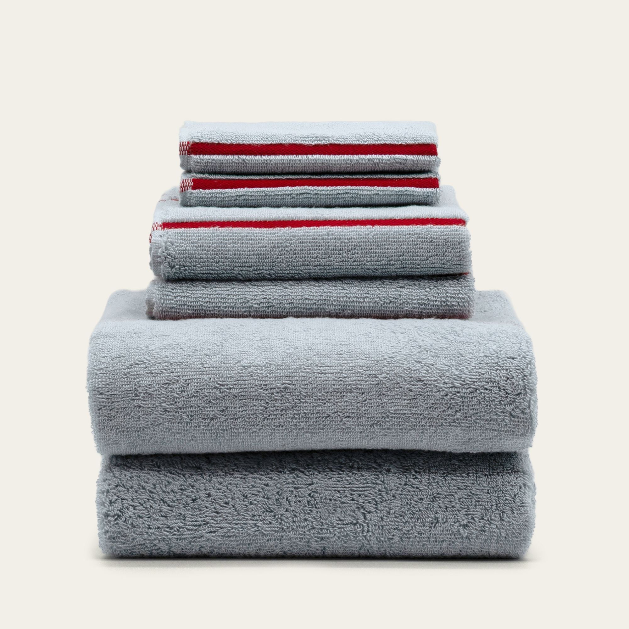 Deia Australian Cotton towels in plush grey terry cotton, stacked in assorted sizes with narrow red stripe details