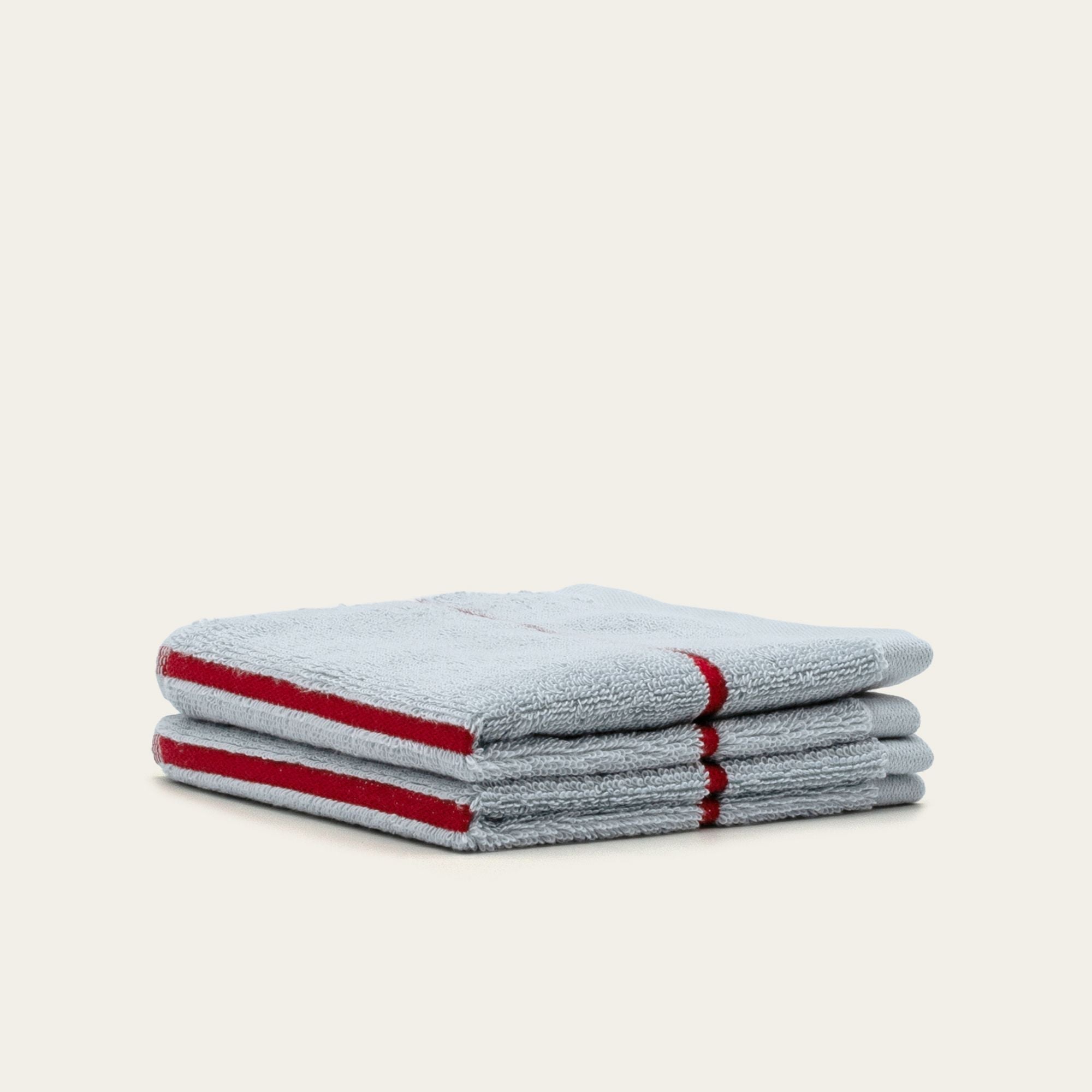 Towels in Deia Australian Cotton, folded in a plush light grey terry weave with bold red stripe edging