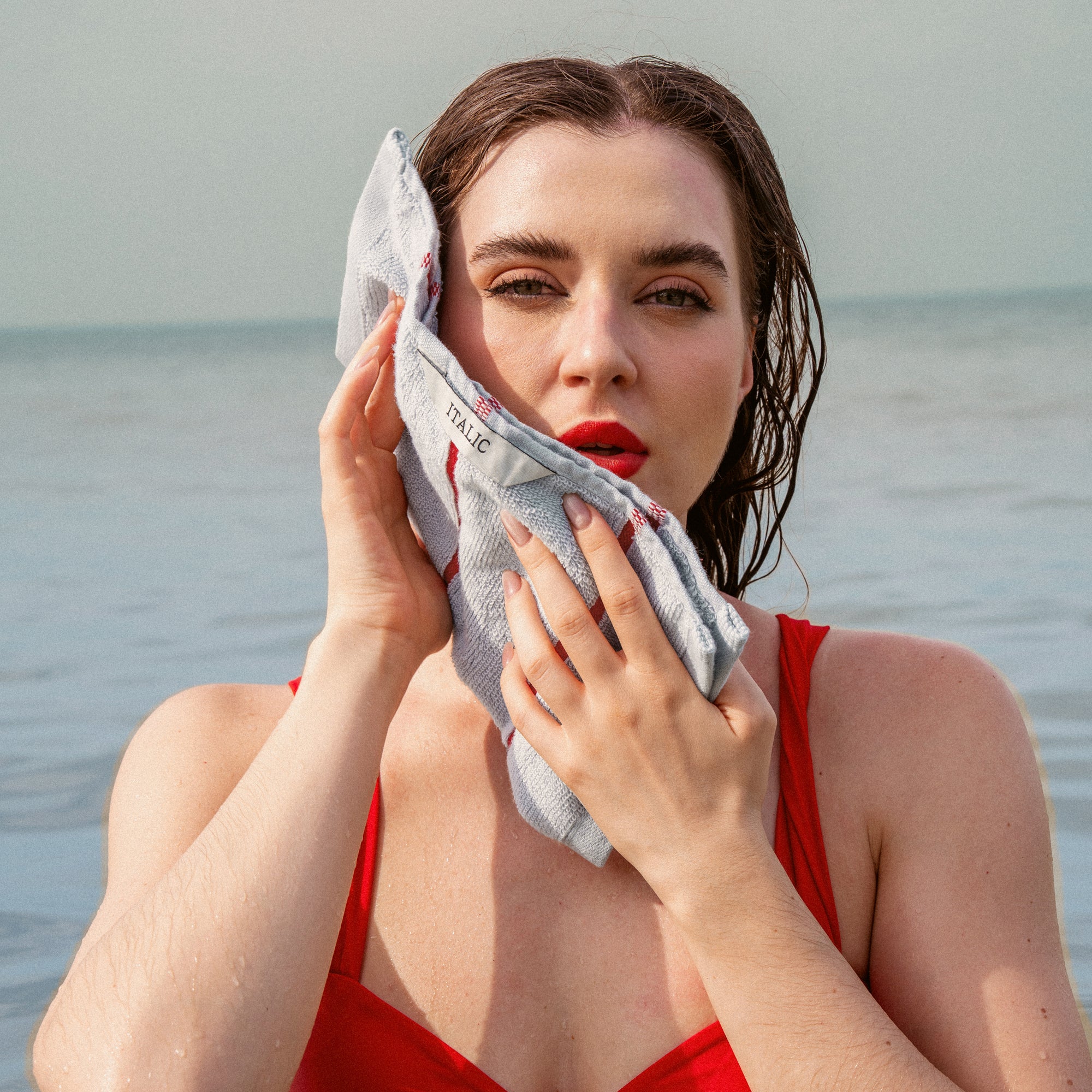 Deia Australian Cotton towel in pale grey with a subtle woven pattern, held against a woman's face