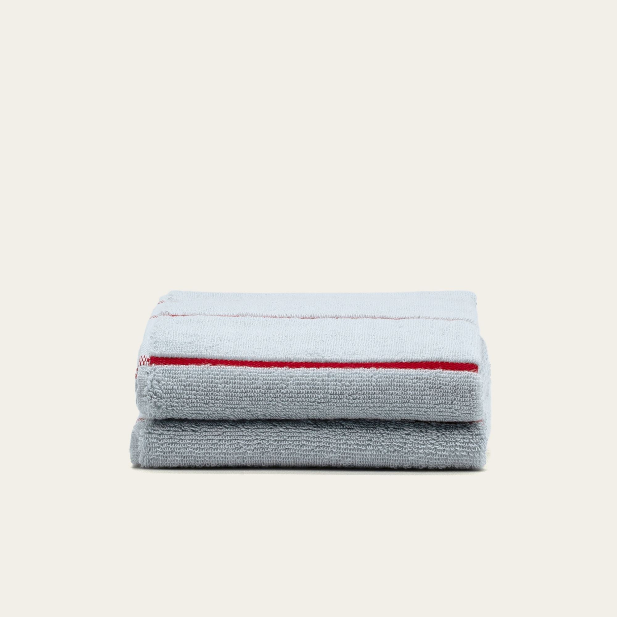 Deia Australian Cotton towels in white and light gray, plush cotton terry with a bold red stripe along the edge