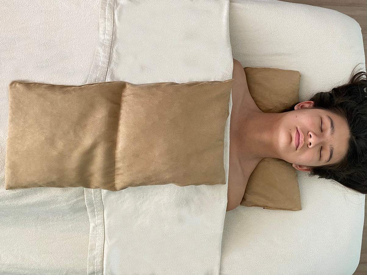 Double Square Cherry Stone Pillow in tan ultra-suede, with a soft rectangular shape shown warming a person's torso