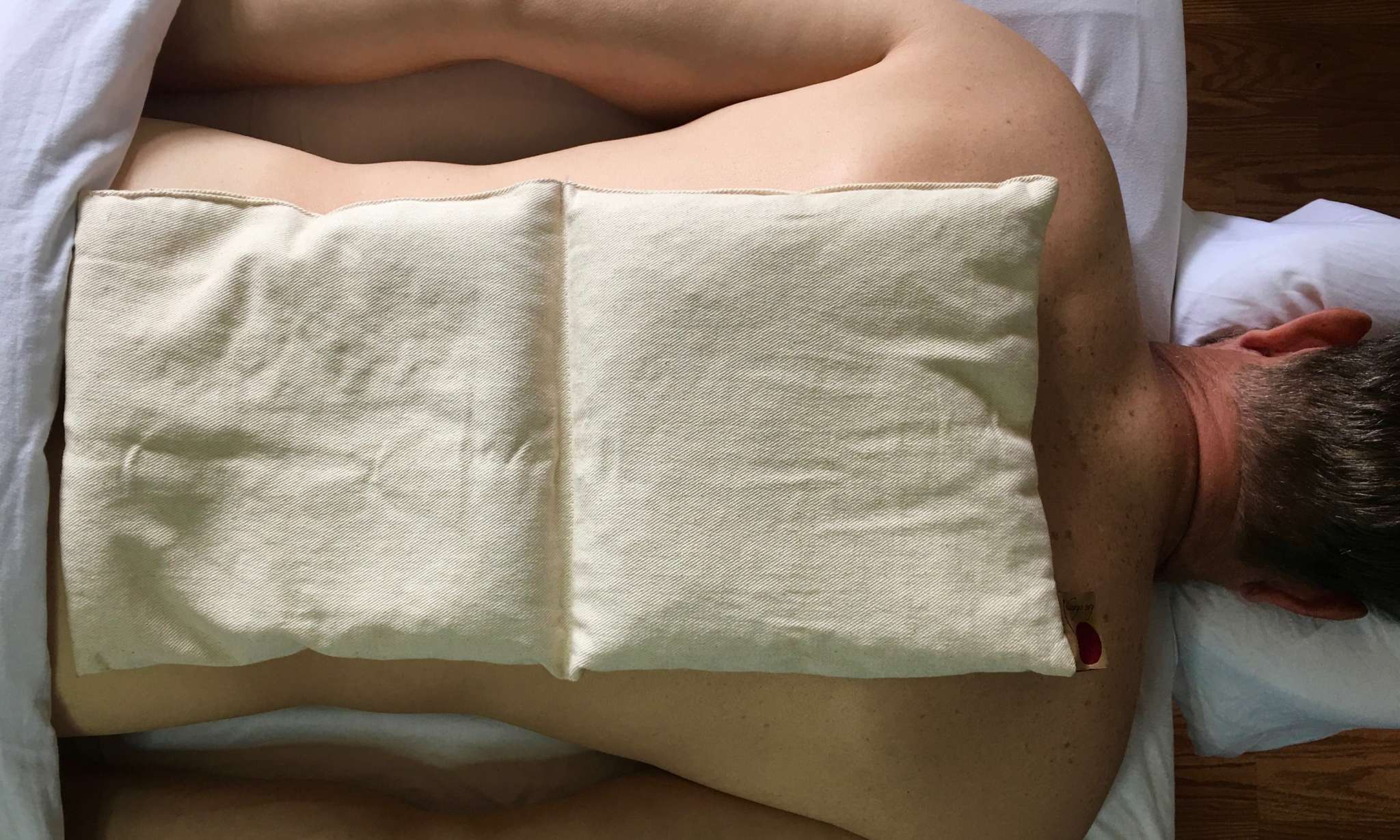 Double Square Pillow in off-white natural fabric, formed from two joined rectangular sections and resting across a person's back