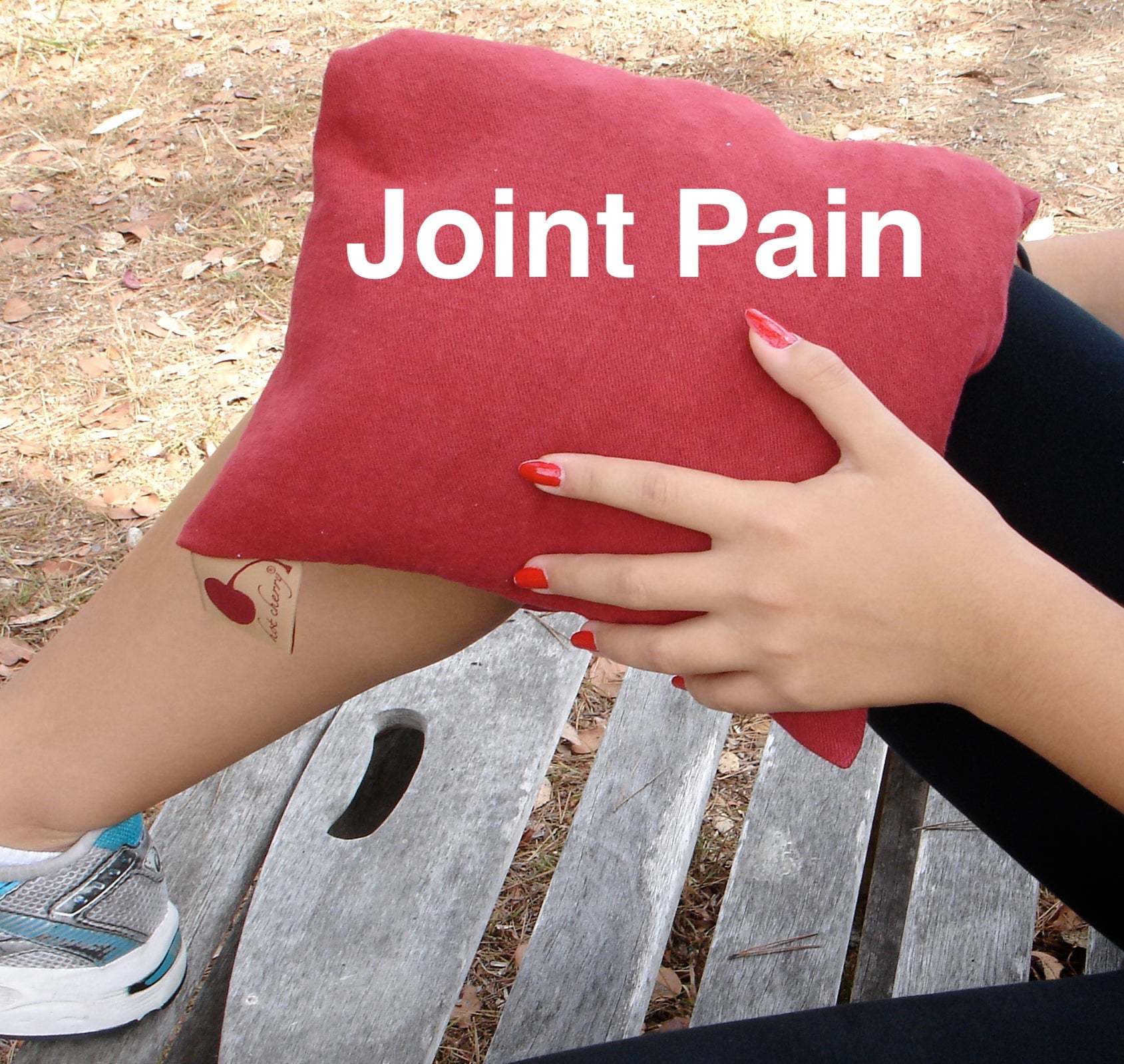 Double Square Pillow in red plush fabric, held against a knee with white “Joint Pain” lettering across the front