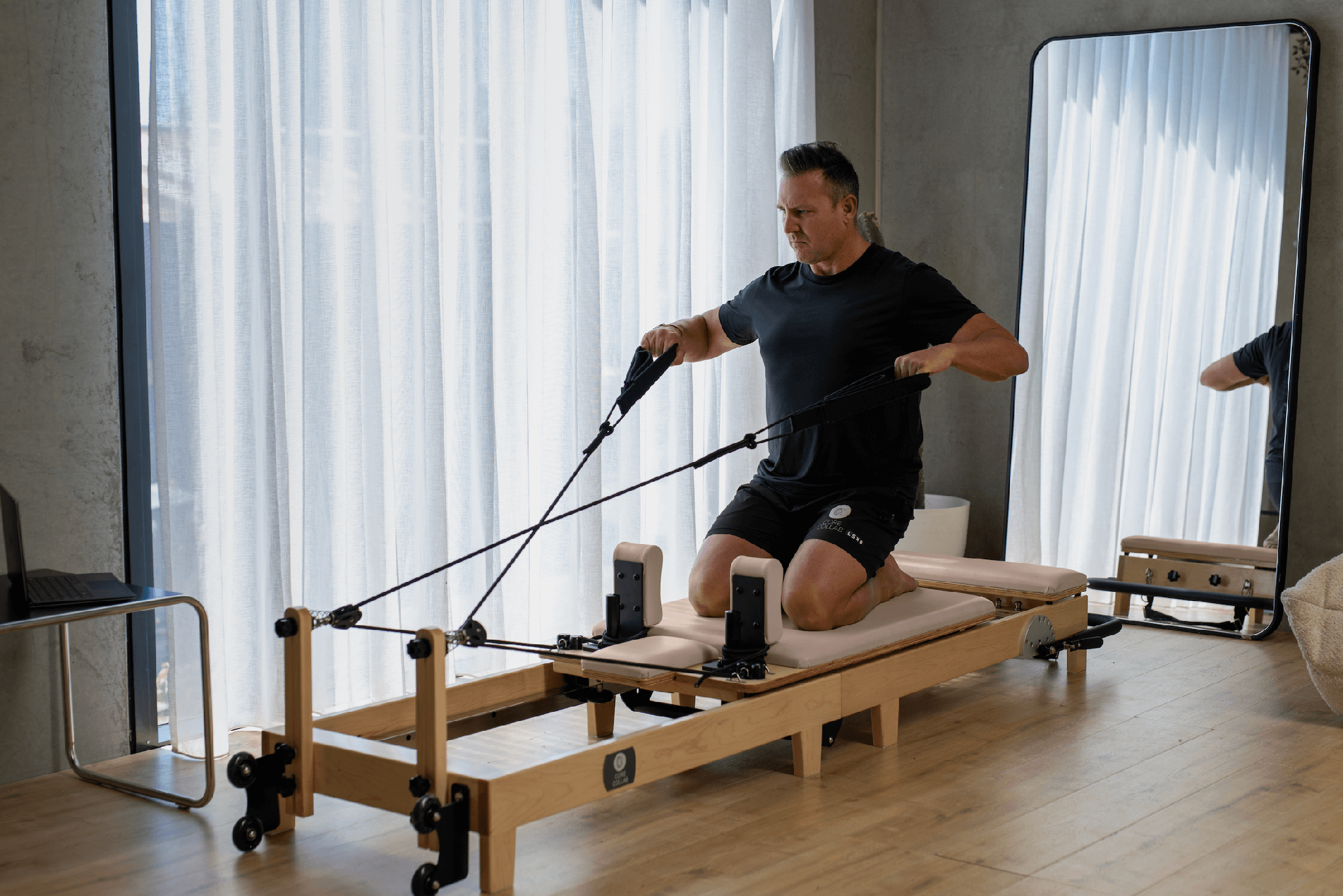 Eco Folding Pilates Reformer with a natural maple wood frame, beige padded carriage, black straps and adjustable footbar.