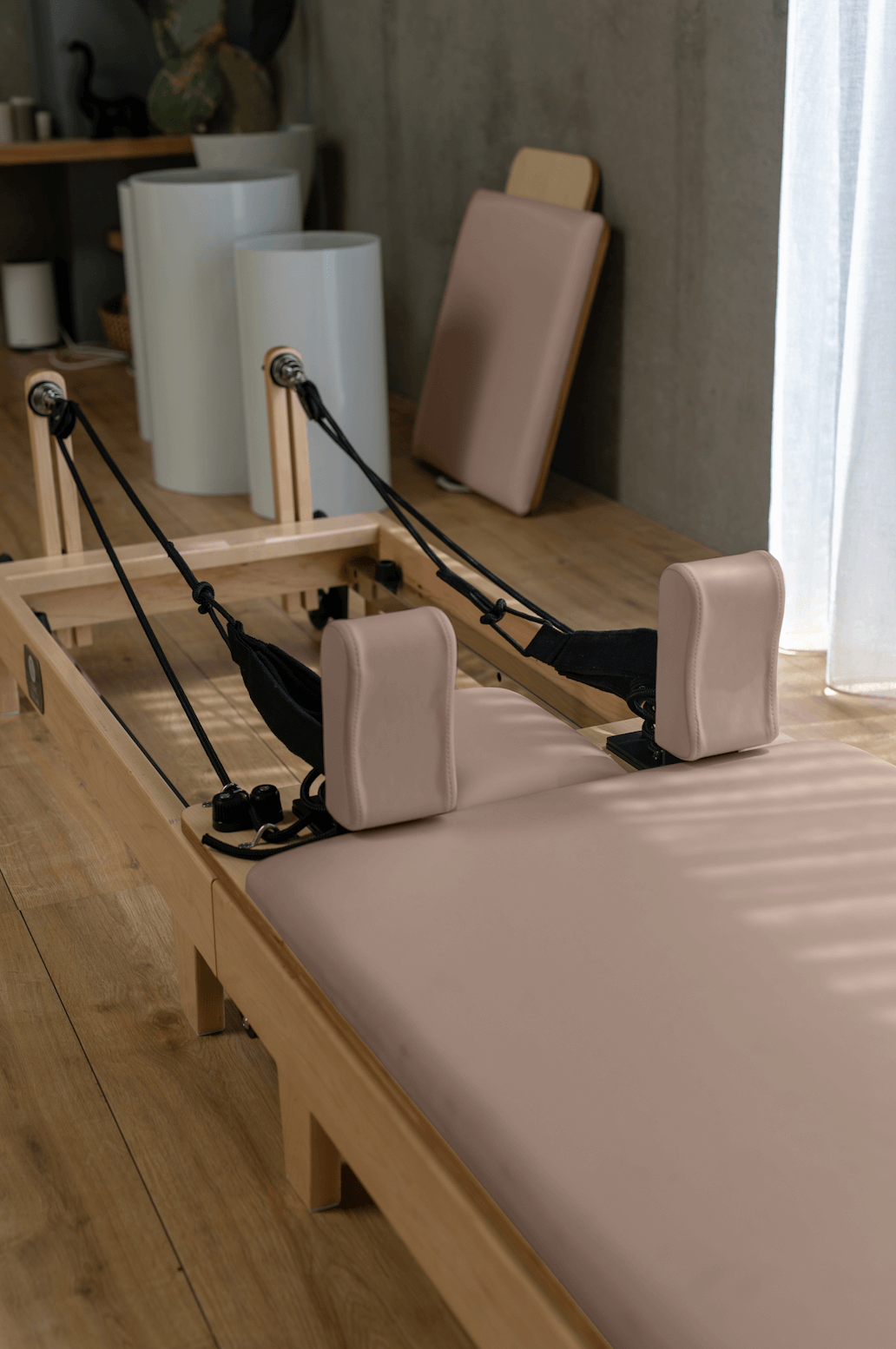 Eco Folding Pilates Reformer with a pale maple wood frame, blush pink padded carriage and matching shoulder rests