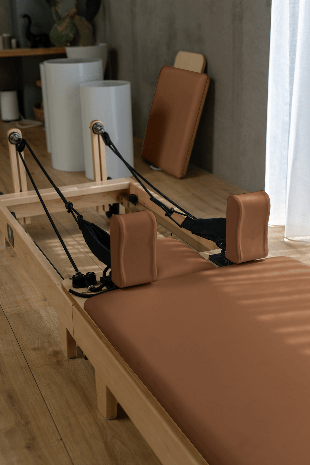 Eco Folding Pilates Reformer with a natural maple wood frame, caramel-brown padded carriage, and black straps